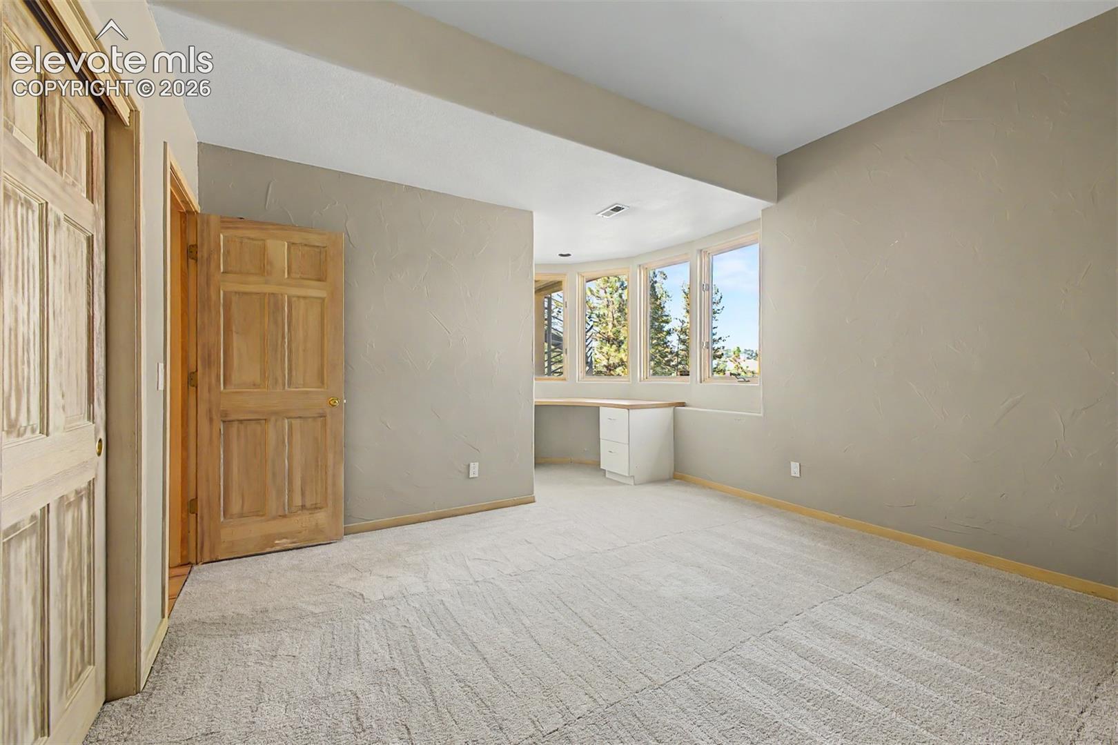 Carpeted room with a built-in desk, bay windows, and wood panel doors