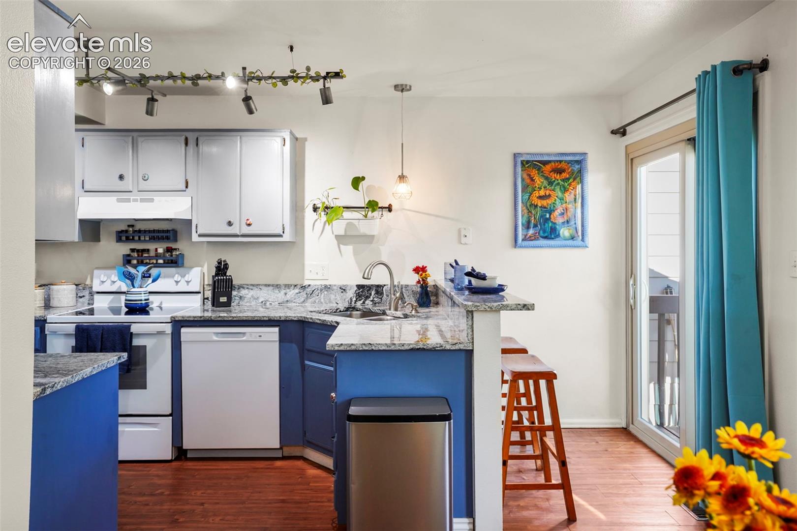 Kitchen featuring multi-tone cabinetry, stone-surface countertops, wood-finish flooring, track lighting, and a sliding glass door