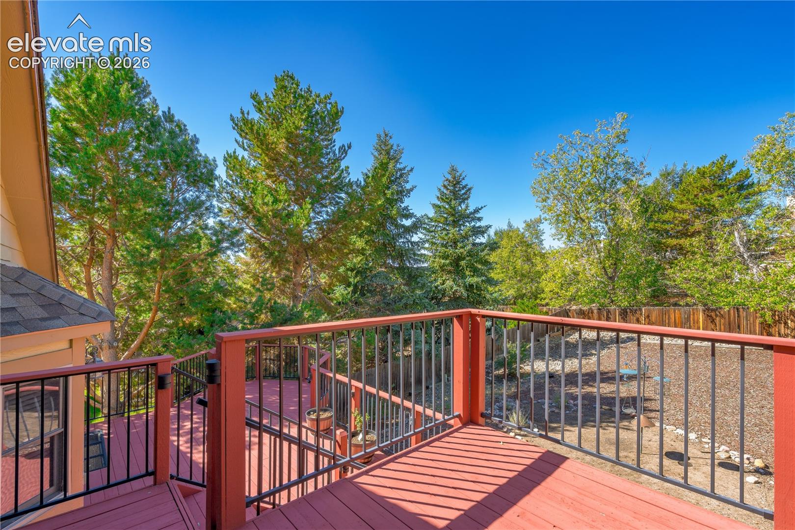 Expansive multi-level deck with red-stained wood and black metal railings, overlooking a landscaped yard with mature trees