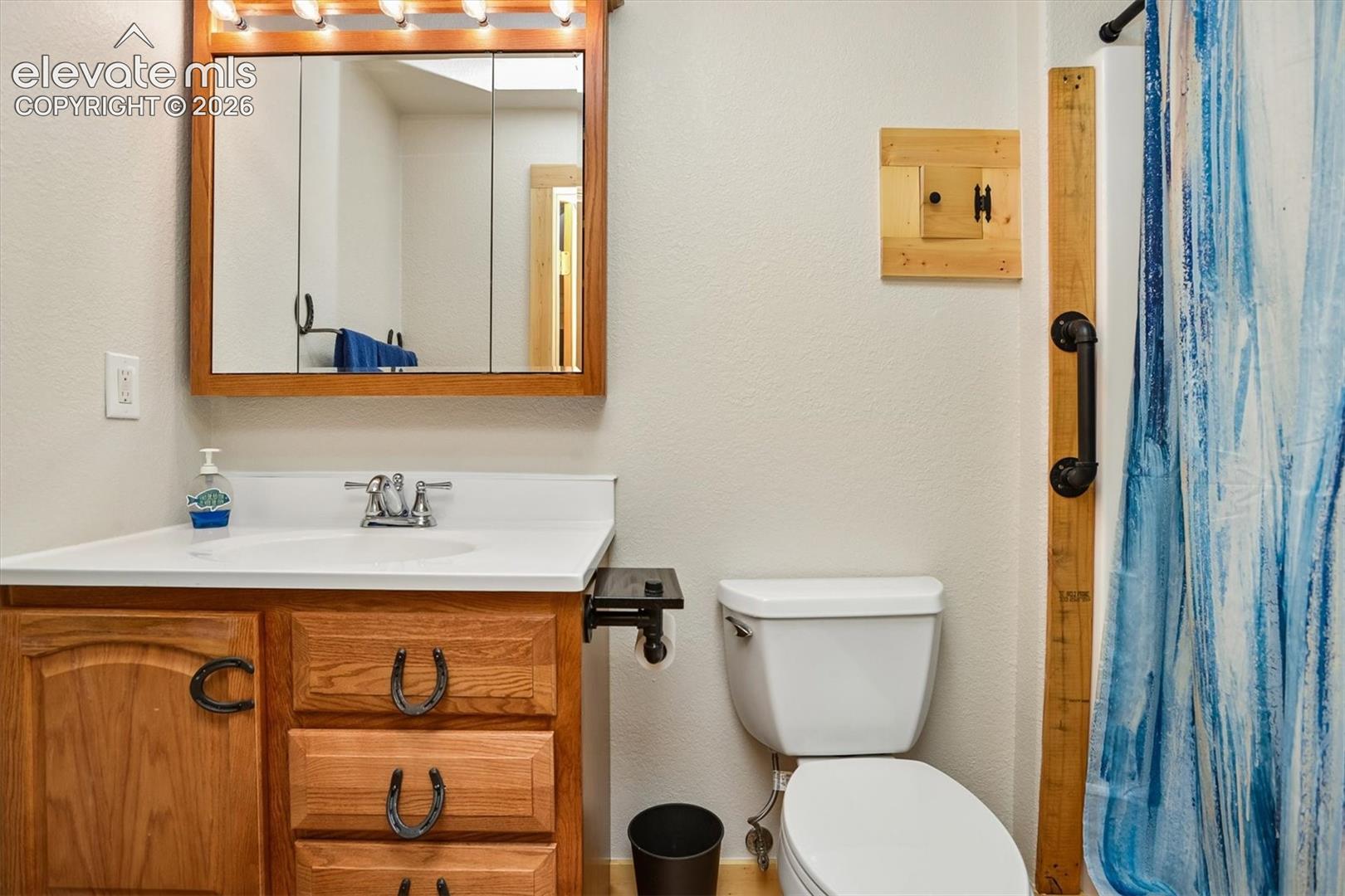 Bathroom vanity featuring a wood-finish cabinet with horseshoe-shaped hardware, a white countertop, and an integrated sink with a chrome faucet