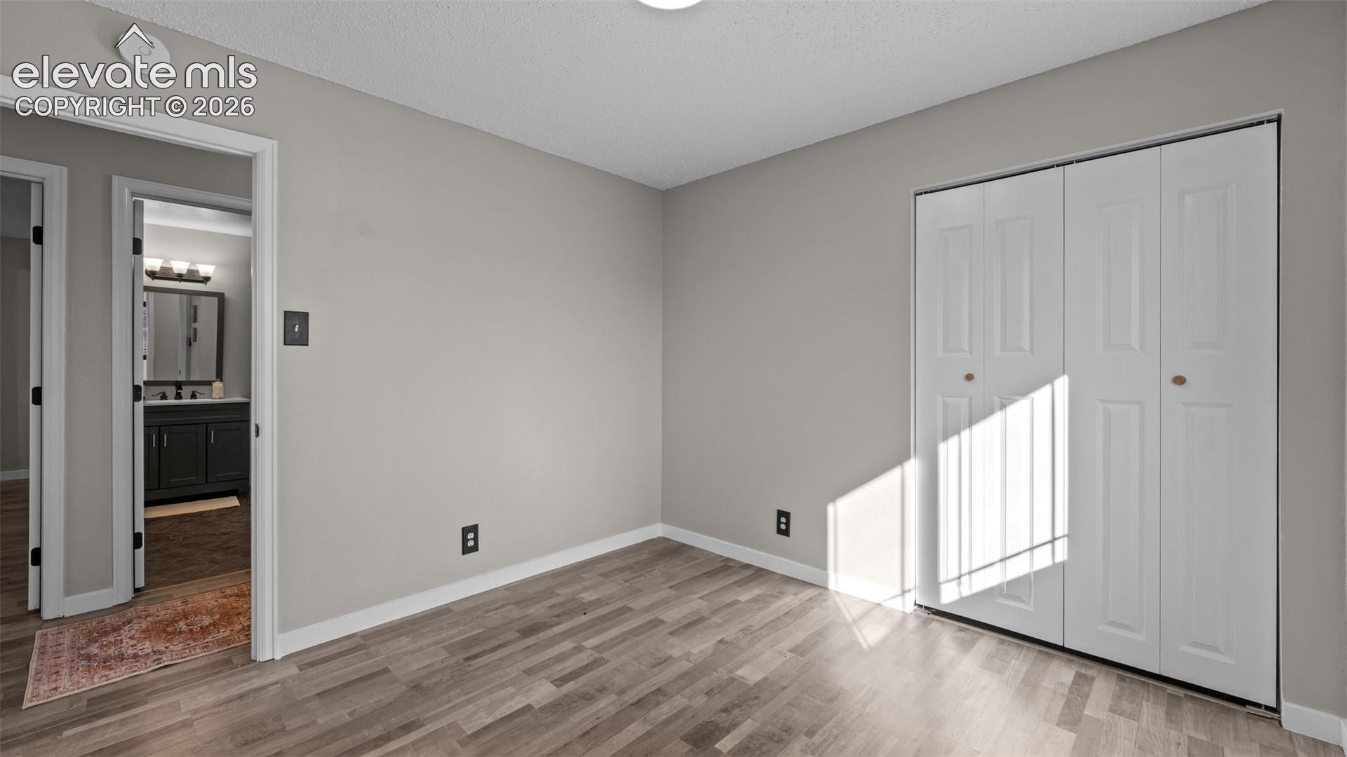 Room featuring wood-finish flooring, neutral wall paint, and a built-in closet with white paneled bi-fold doors