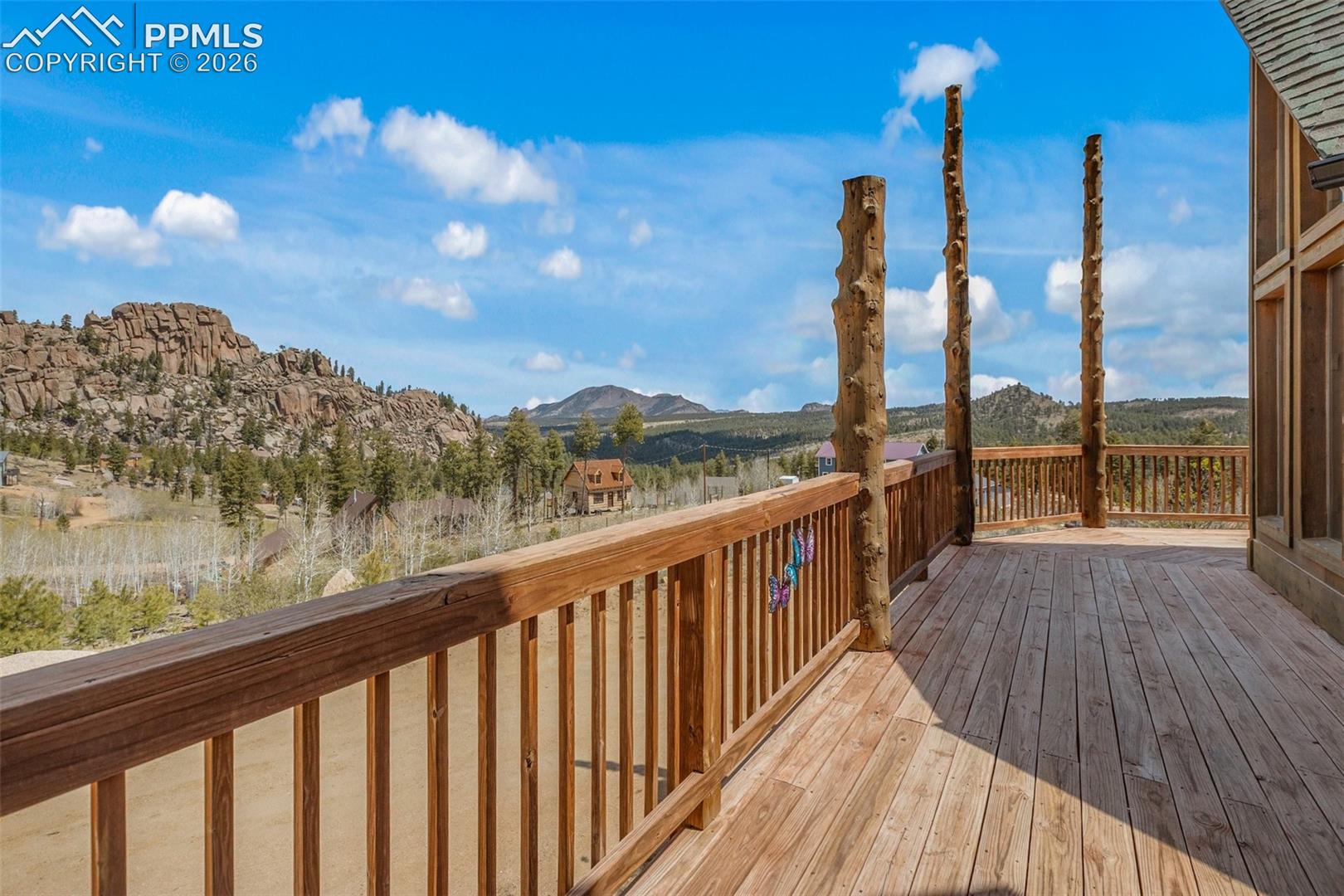 Expansive outdoor deck featuring wood flooring and railings, natural wood support posts, and large vertical windows