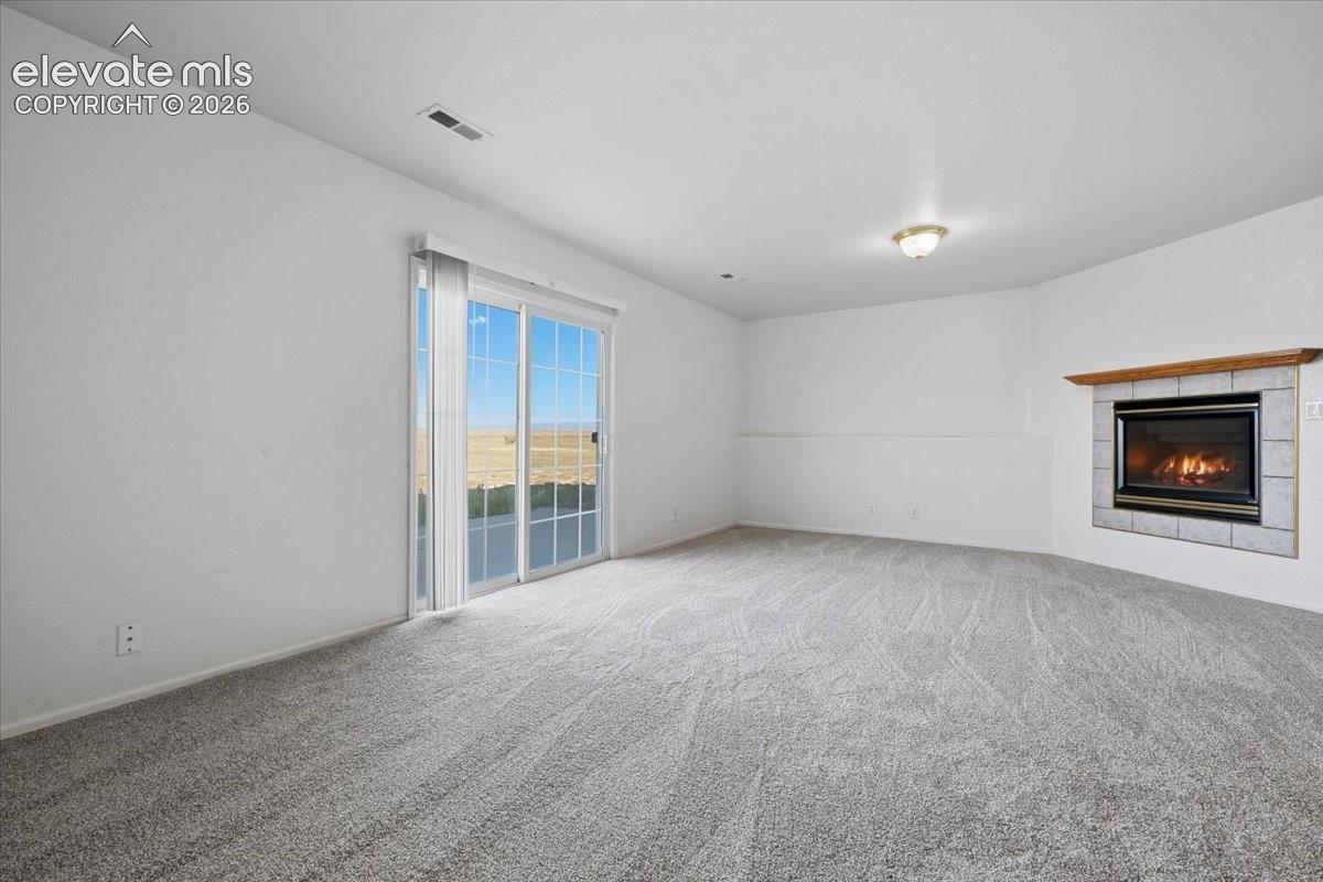 Carpeted living space featuring a fireplace with a tile surround and wood mantel, a sliding glass door, and a flush mount light fixture