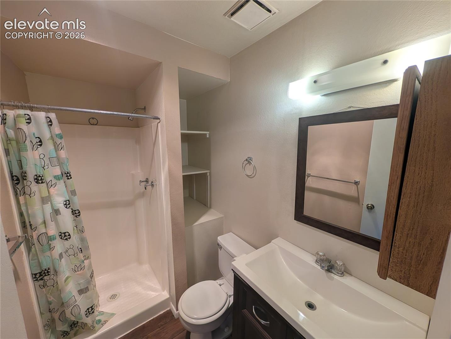 Bathroom featuring a vanity with an integrated sink, framed wall mirror, built-in shelving, and a shower with a white surround