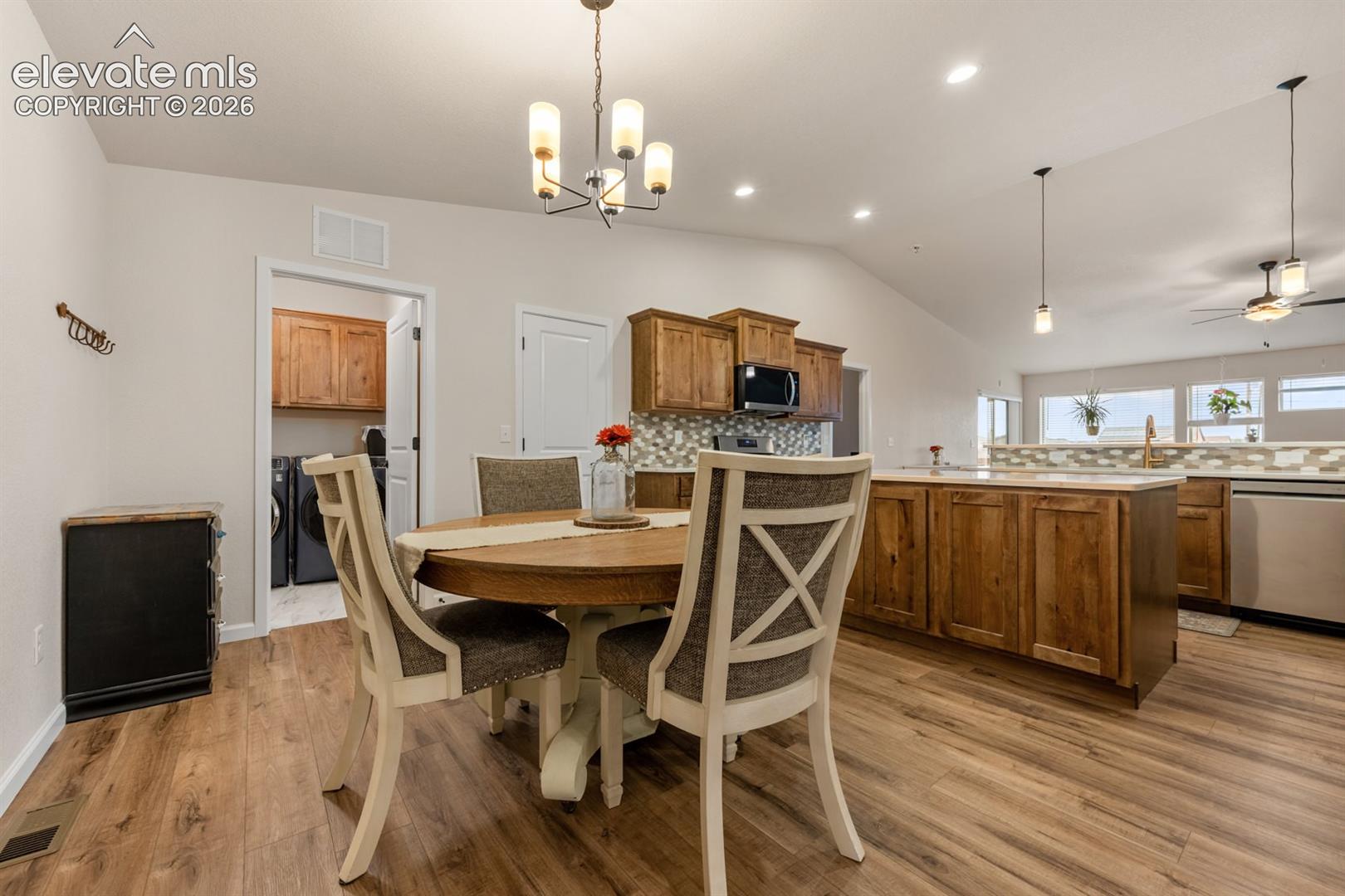 Kitchen featuring wood cabinetry, a center island with countertop seating, stone-tiled backsplash, vaulted ceilings, and wood-finish flooring