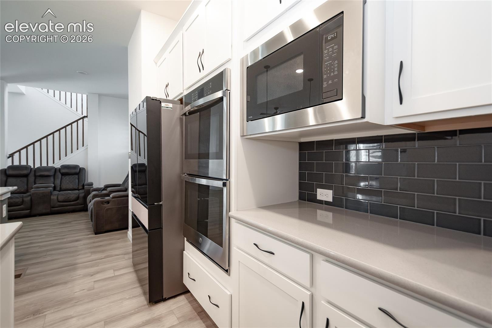Kitchen featuring white cabinetry, solid surface countertops, a dark-toned subway tile backsplash, stainless steel double wall ovens, and a built-in stainless steel microwave