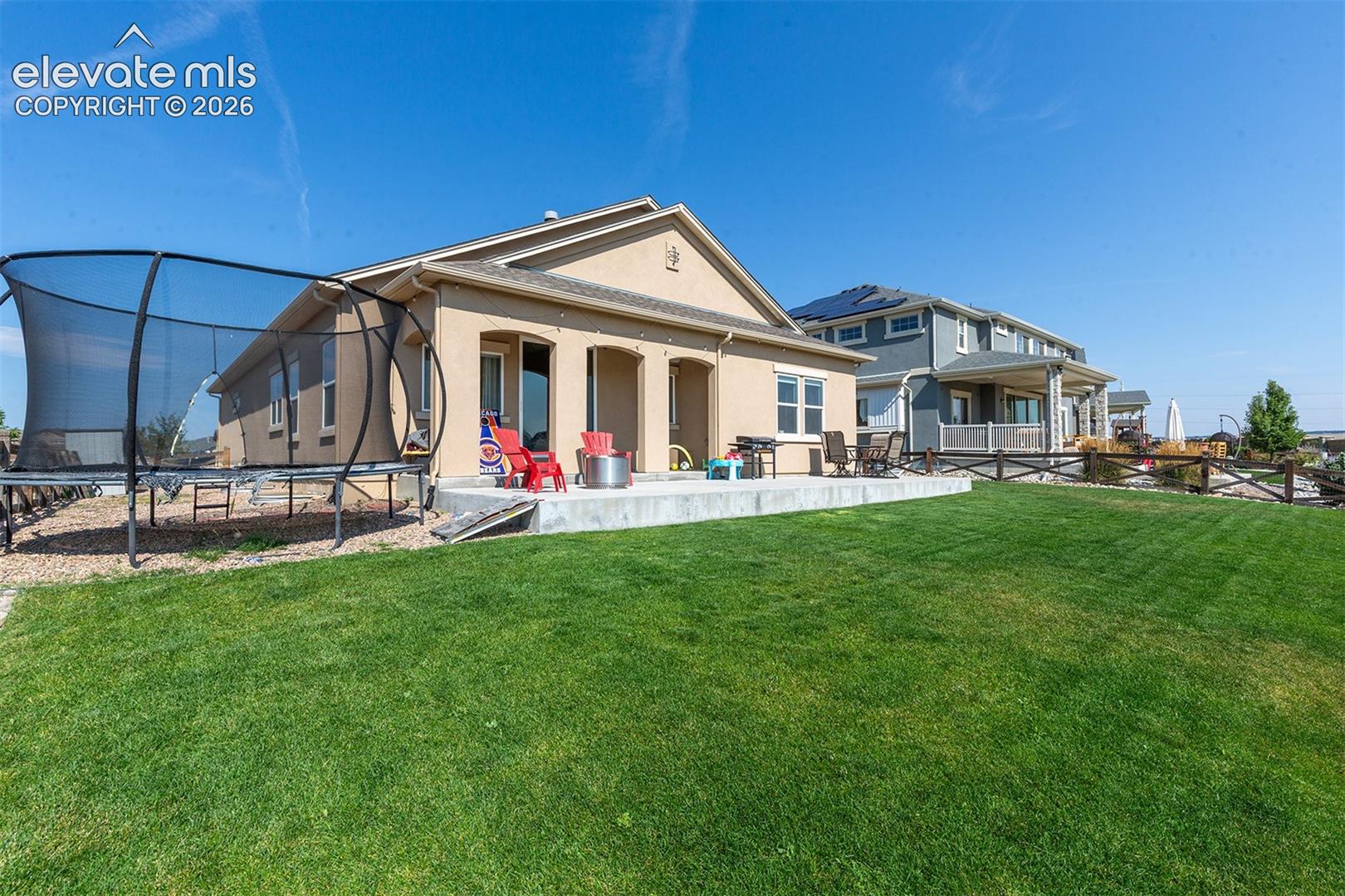 Expansive green lawn with a concrete patio featuring a built-in fire pit, multiple sliding glass doors, and a stucco exterior