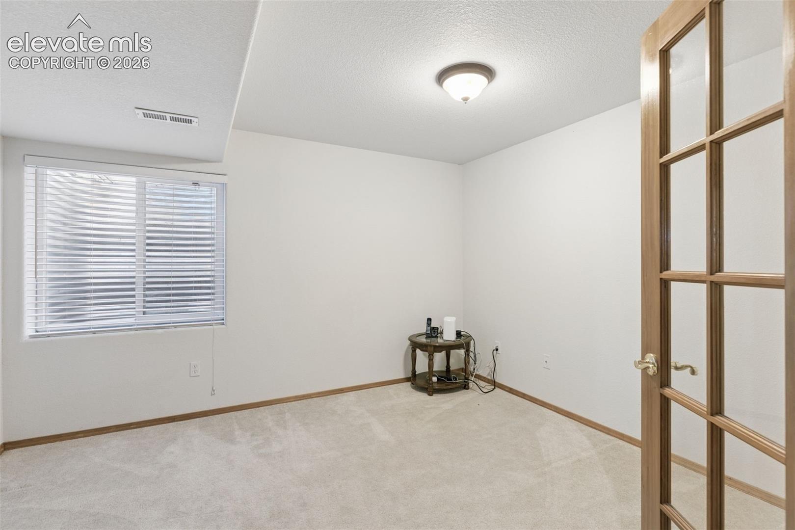French door entry with glass paneling, neutral carpeting, window with integrated blinds, and a flush-mount ceiling light fixture