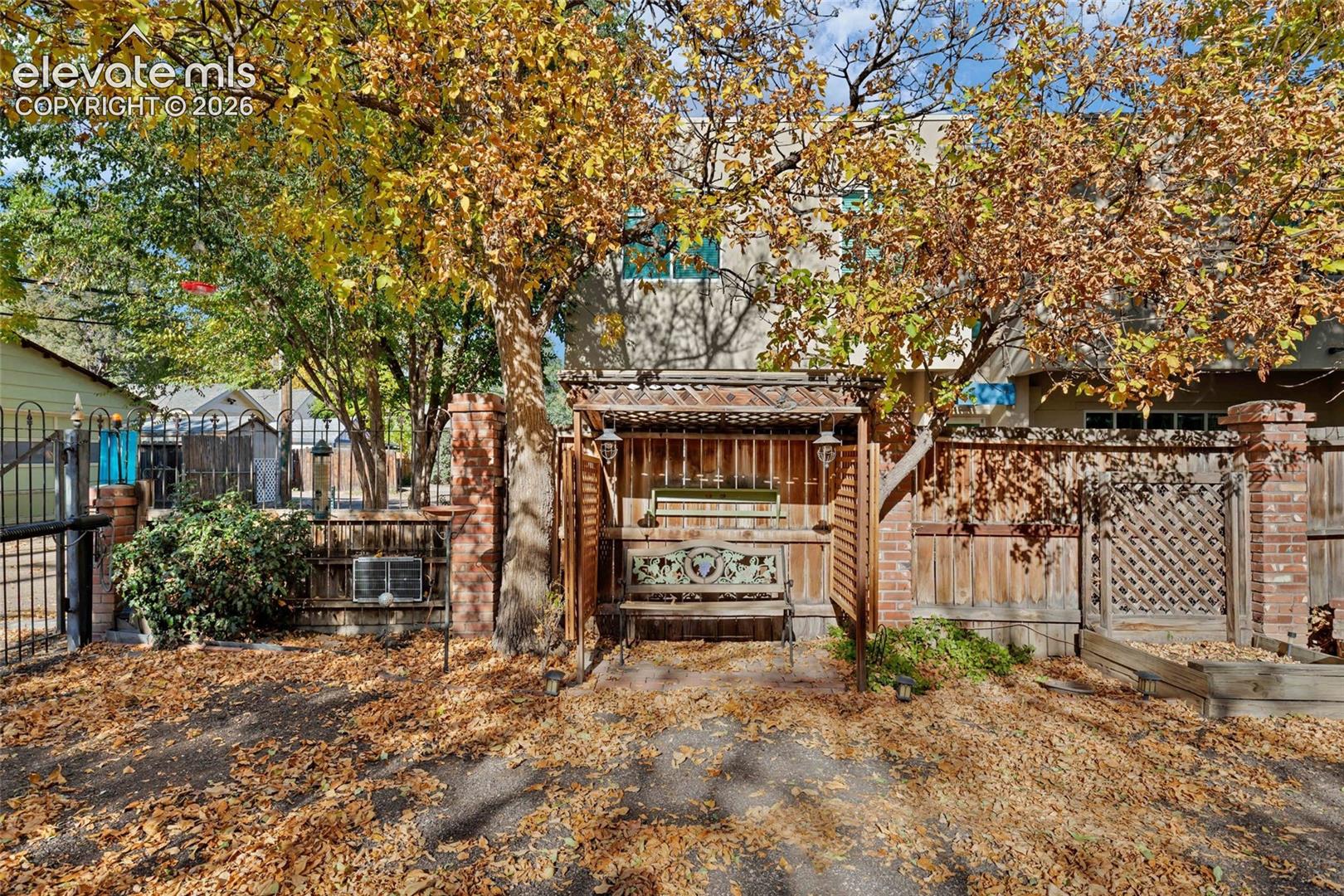 Outdoor space featuring a brick-columned fence, a wooden pergola structure, lattice paneling, and mature trees
