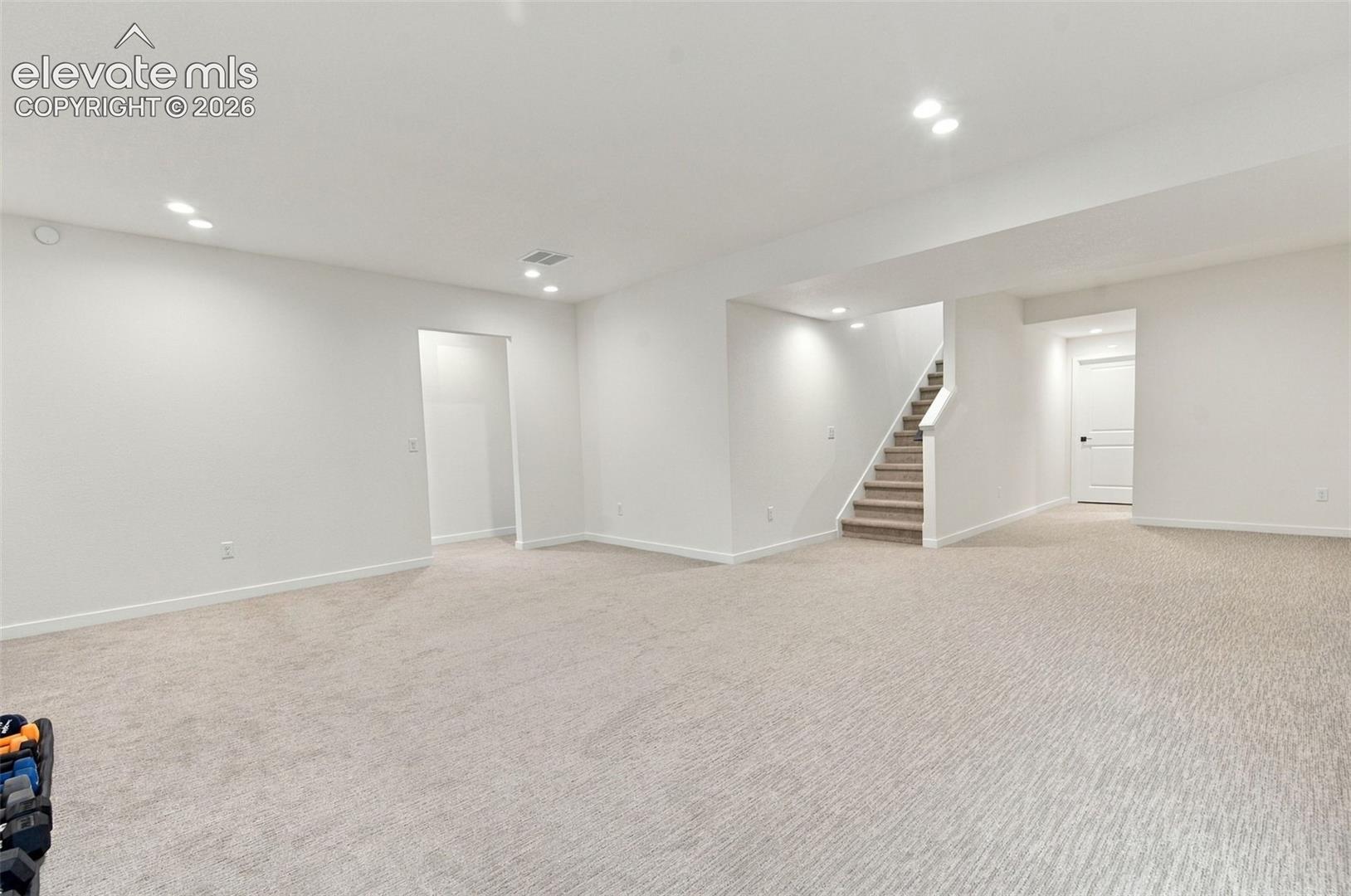 Open floor plan featuring neutral carpeting, recessed ceiling lighting, and a staircase with a white handrail