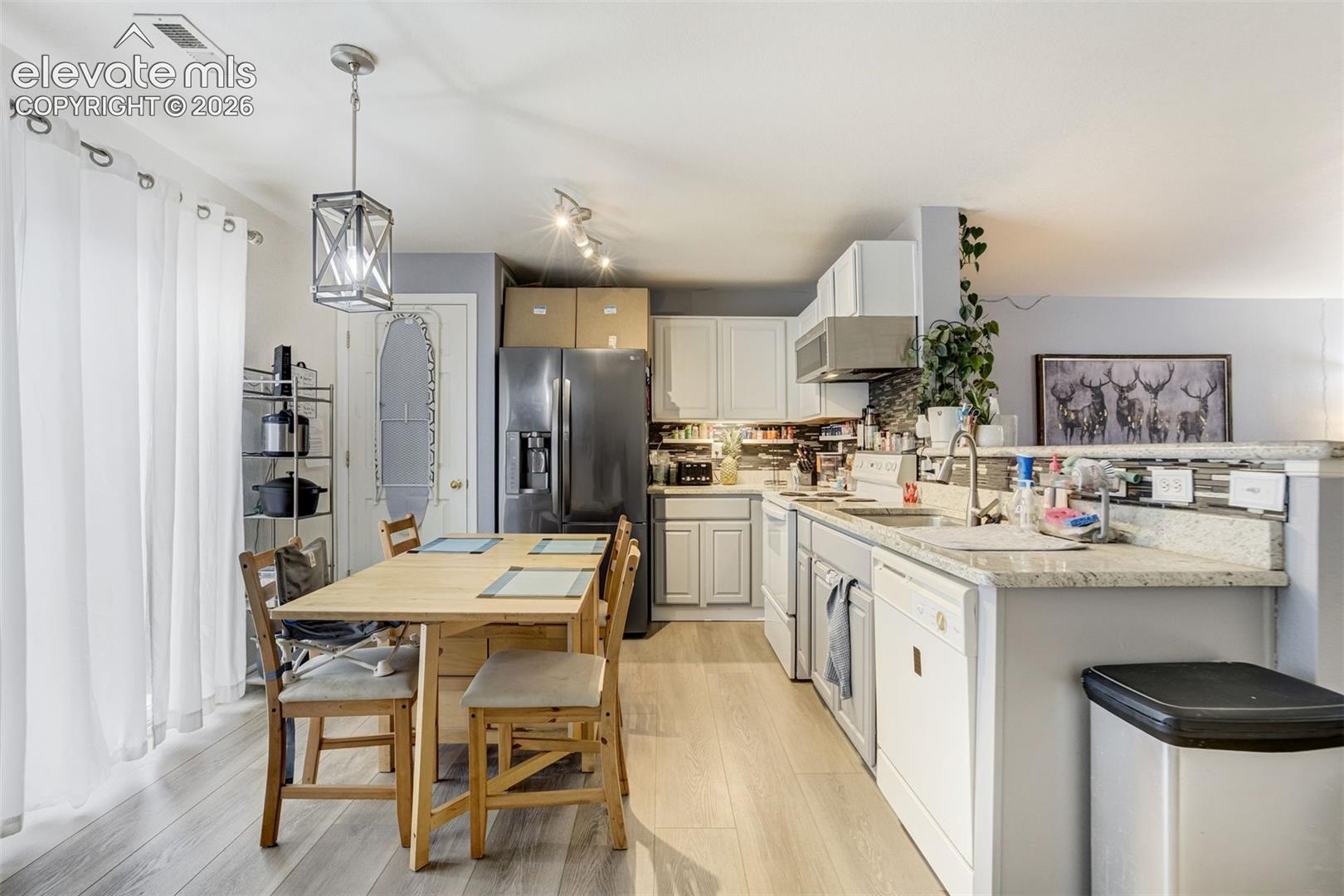 Contemporary kitchen featuring light wood-finish flooring, white cabinetry, granite-style countertops, a stainless steel range hood, and track lighting