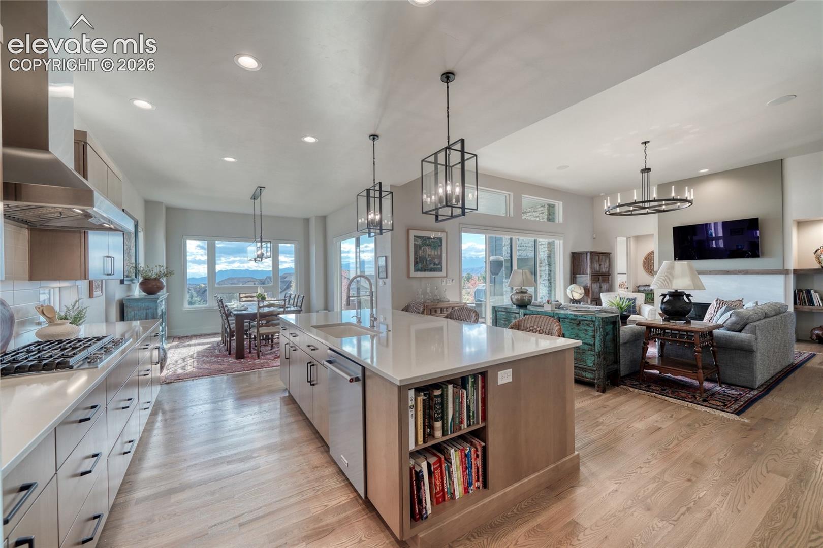 Open-concept kitchen featuring an expansive center island with stone countertop, stainless steel appliances, custom wood-finish cabinetry, recessed lighting, and geometric pendant fixtures