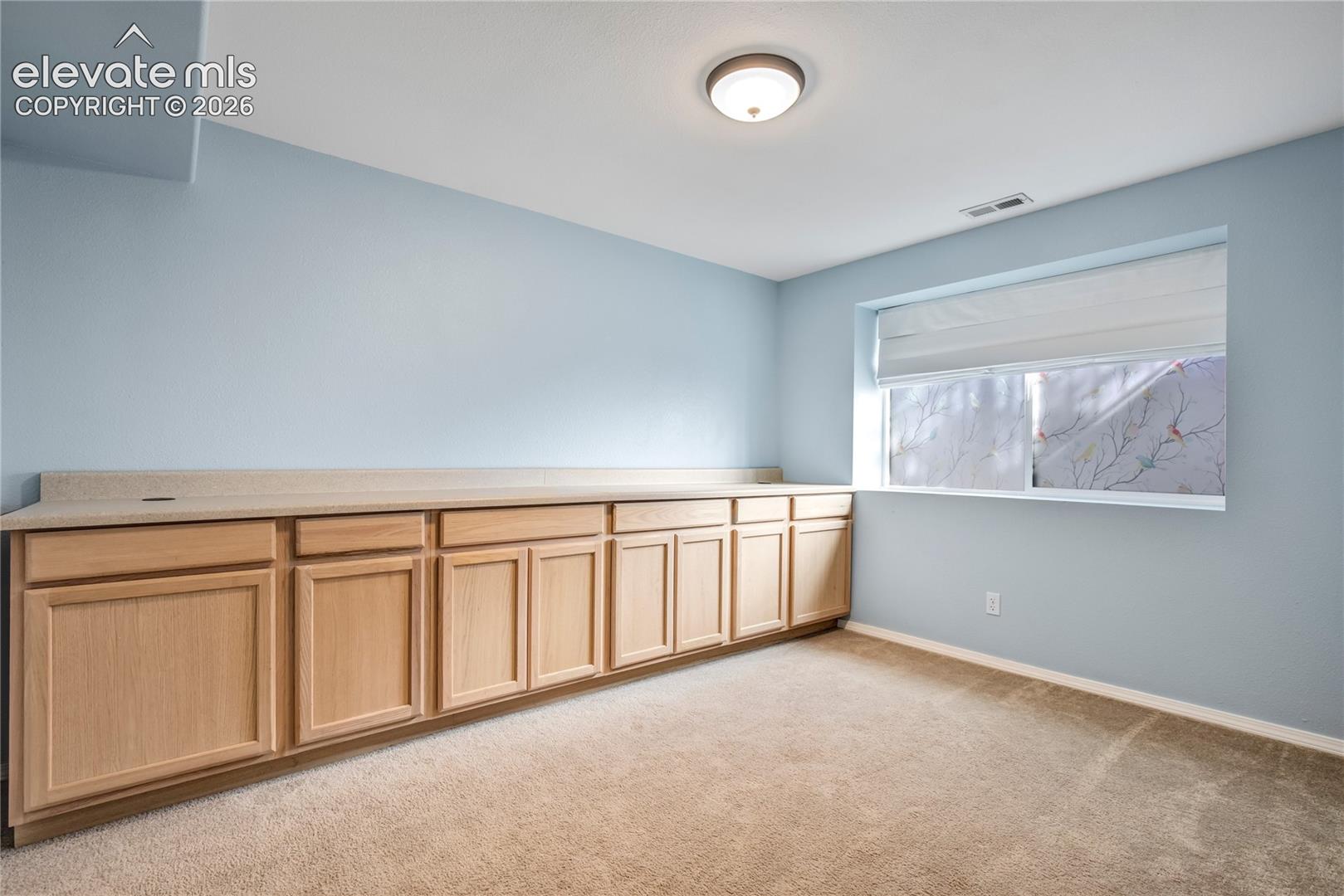 This basement bedroom features an extensive wall of built-in cabinetry + a large window, making it particularly well suited for crafts, hobbies or an organized workspace.