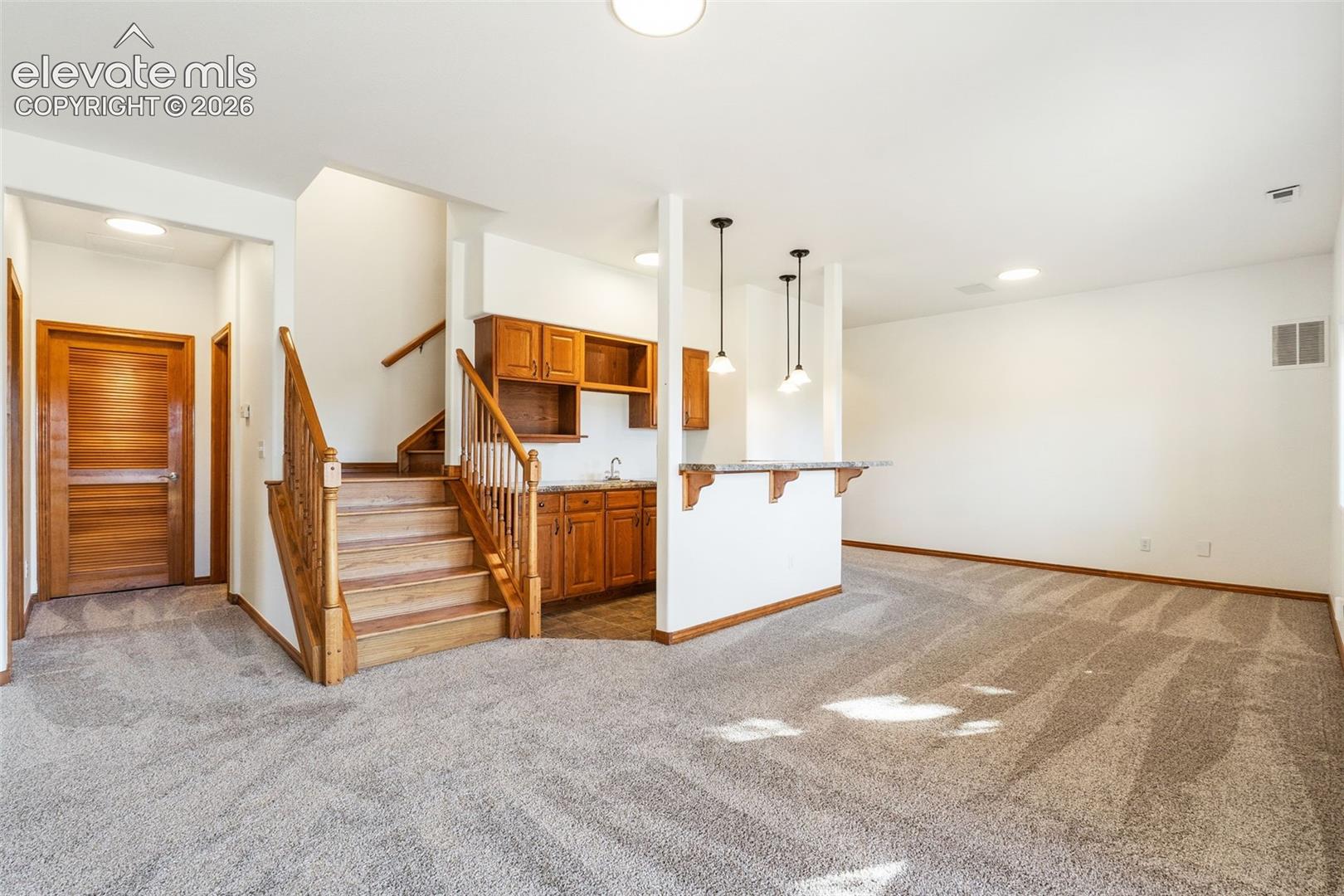 Staircase with wood railings and treads, wet bar featuring wood cabinetry, stone countertops, and hanging pendant lighting