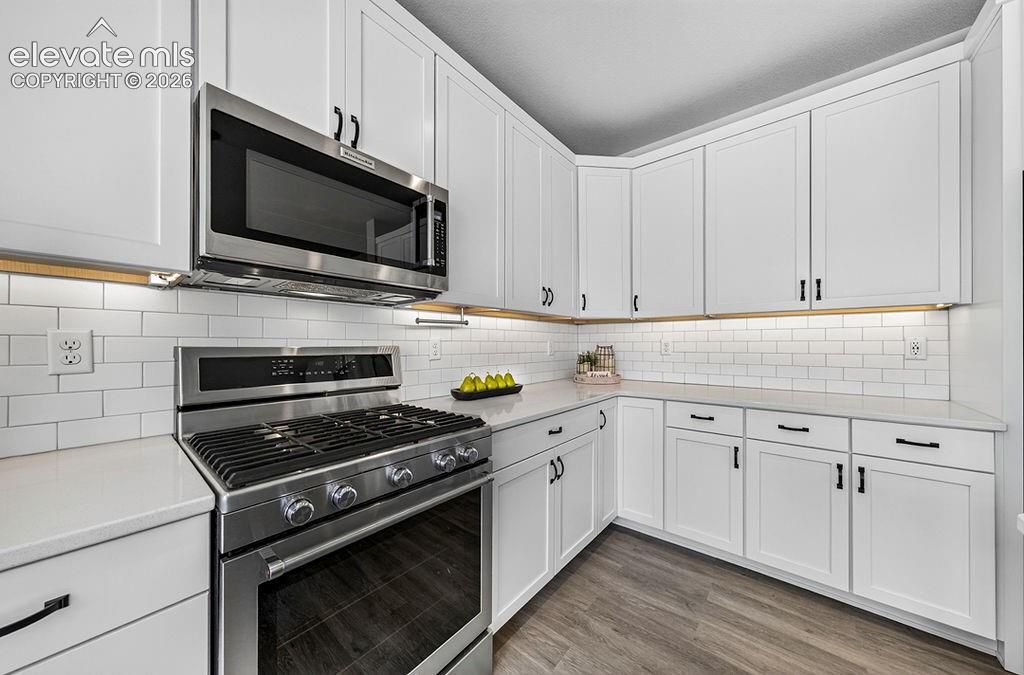 Modern kitchen featuring white shaker cabinetry, stainless steel appliances, light-toned countertops, subway tile backsplash, and wood-finish flooring