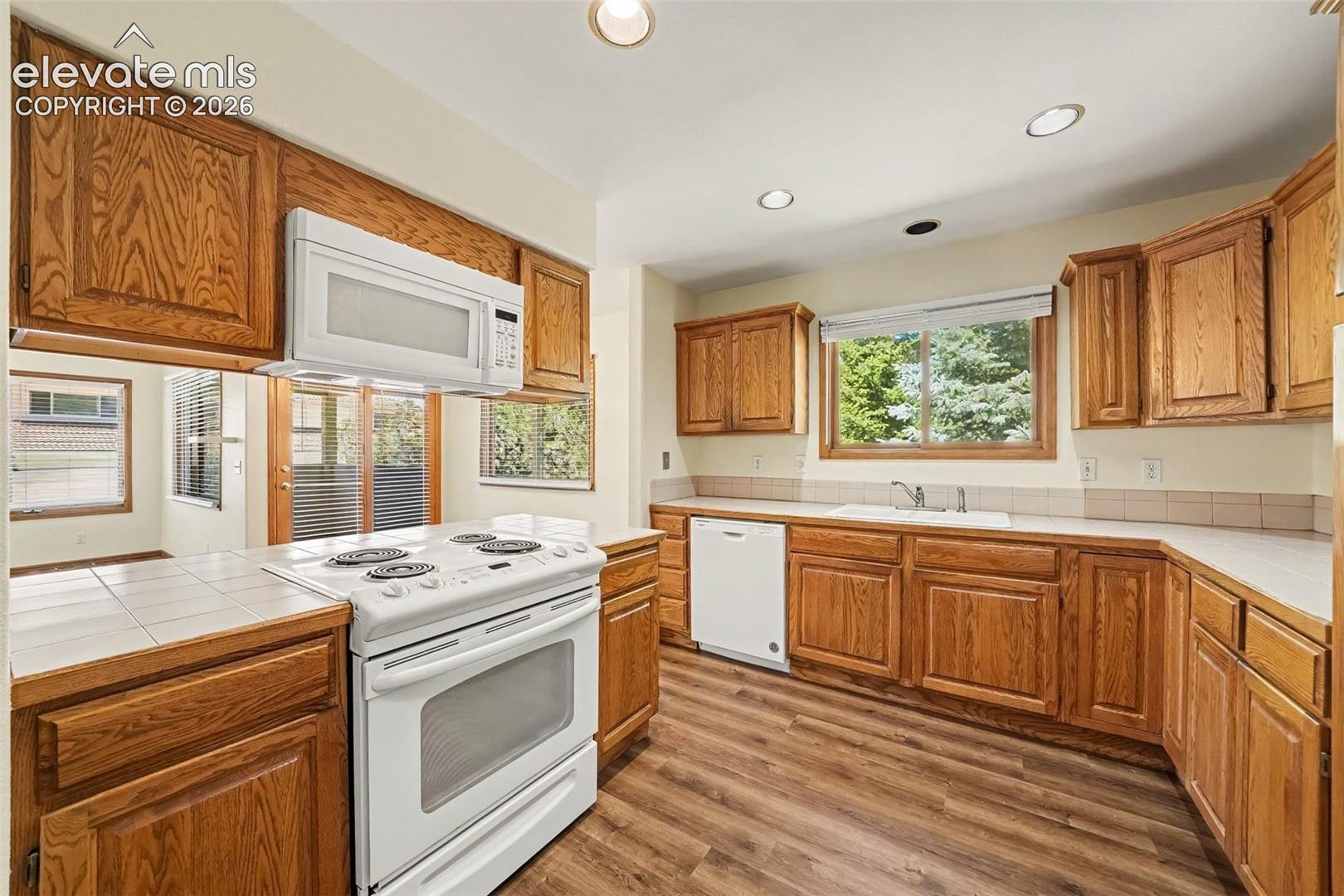 Kitchen featuring wood-finish cabinetry, white appliances, recessed lighting, tile countertops, and new LVP flooring