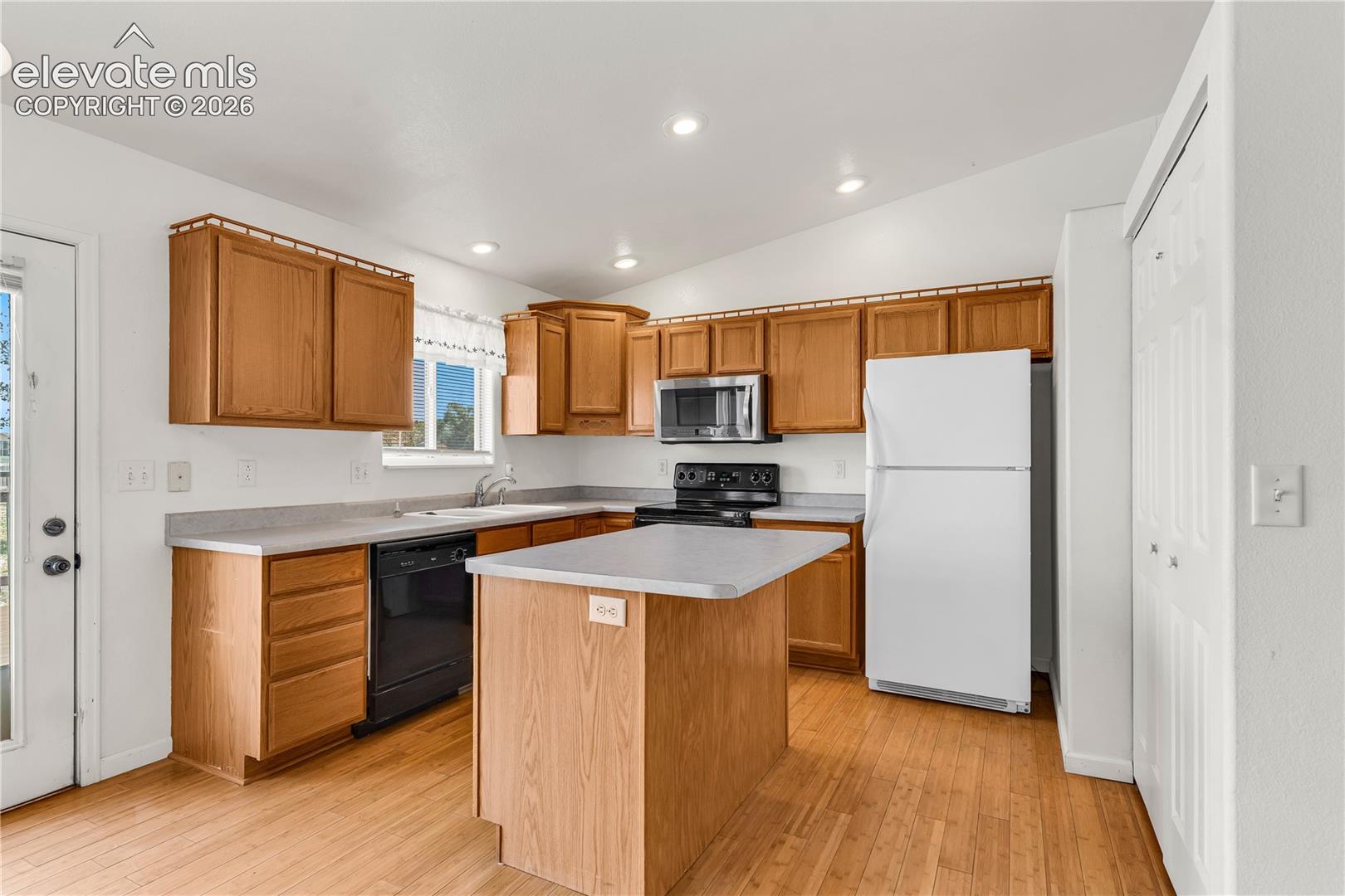 Kitchen featuring wood-finish flooring, wood cabinetry, a center island, and stainless steel microwave