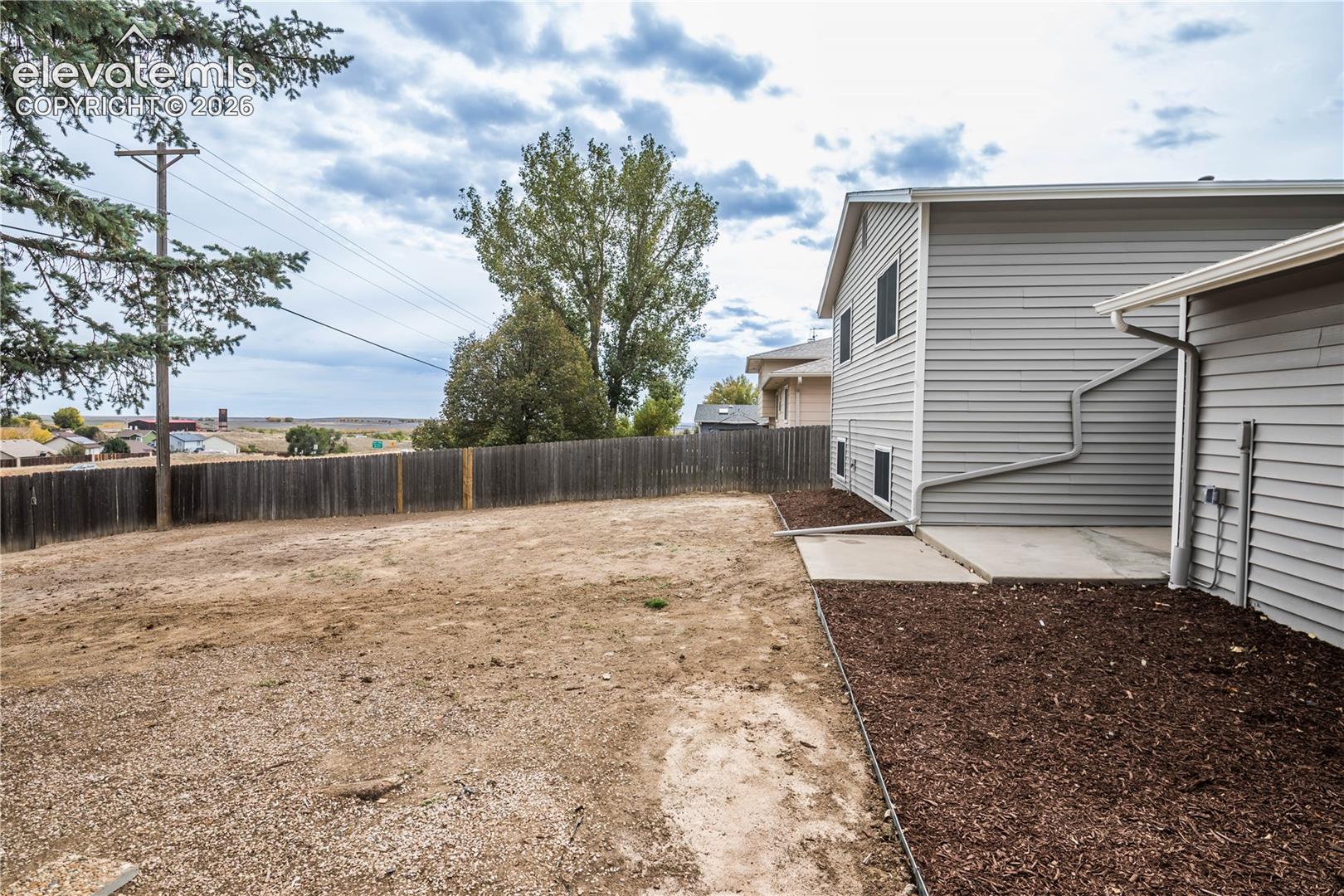 Backyard area featuring horizontal siding, a concrete patio, wood-material fencing, and mulch landscaping beds