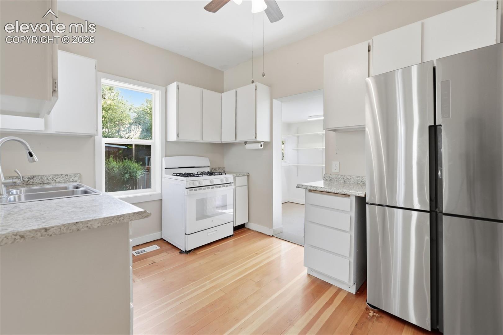 Kitchen featuring pine hardwood flooring, stainless steel refrigerator, white cabinetry, white gas range, a ceiling fan, and light-toned countertops.