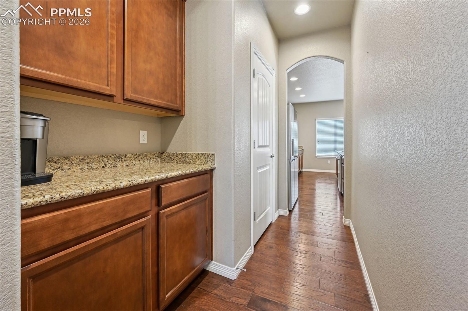Corridor featuring arched walkways, dark wood-style floors, recessed lighting, and a textured wall