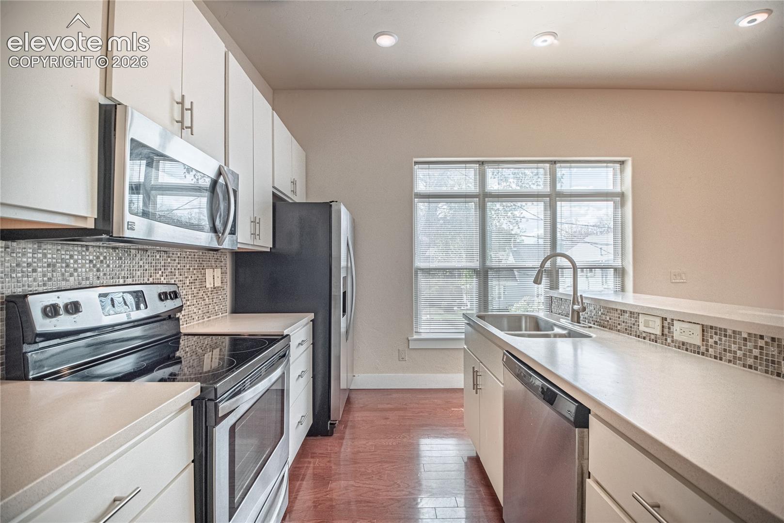 Kitchen featuring light cabinetry, stainless steel appliances, mosaic tile backsplash, wood-finish flooring, and recessed lighting