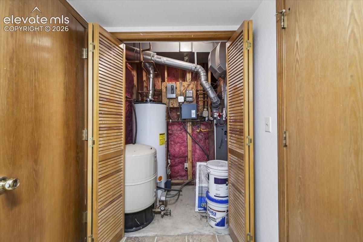 Utility closet featuring bi-fold louvered wood doors, containing a water heater, pressure tank, and mechanical systems