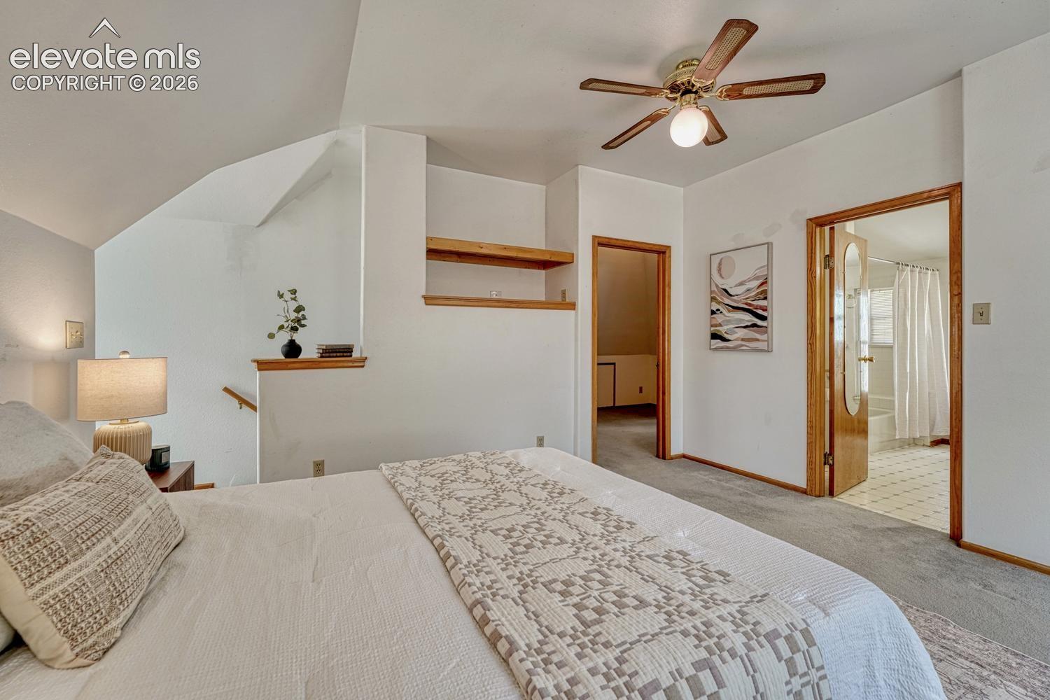 Sloped ceilings, ceiling fan, warm-toned wood trim, built-in shelving, and carpeted flooring
