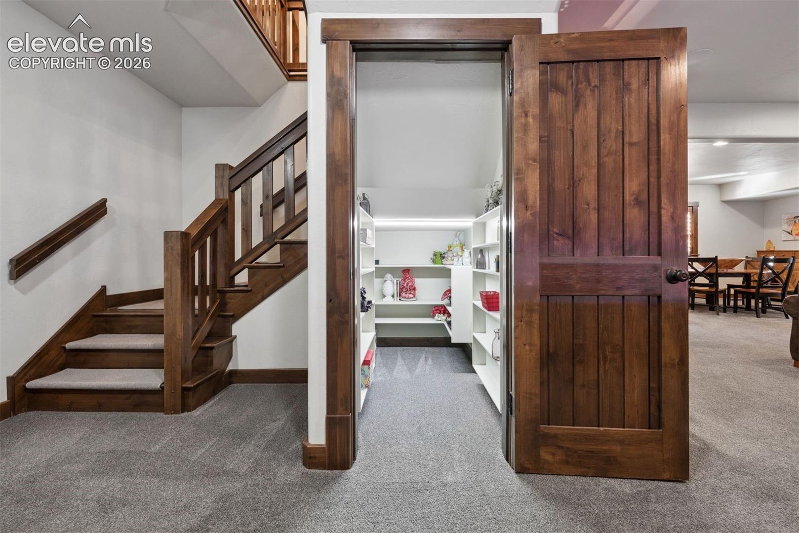 Staircase with wood railings, a dedicated under-stair storage area featuring built-in shelving, and custom wood door casing
