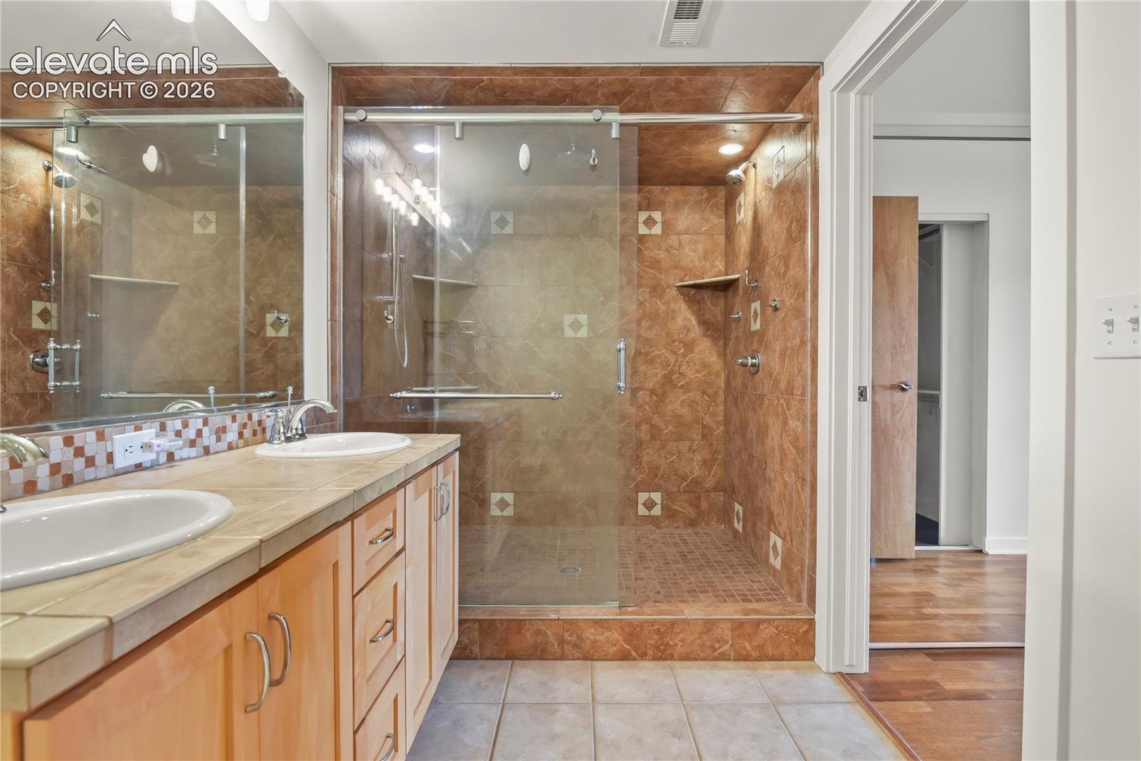 En-suite bath showcasing dual sinks, tile flooring, and oversized shower