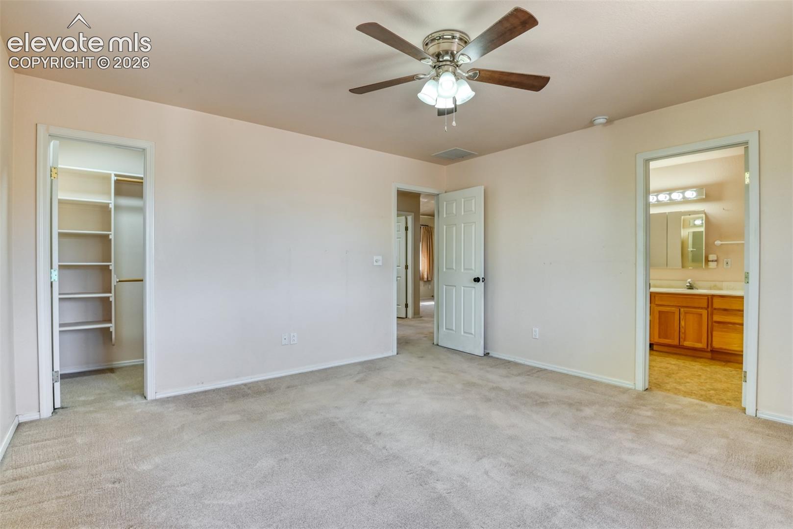 Spacious interior featuring neutral carpeting, a central ceiling fan with integrated lighting, a walk-in closet with built-in shelving, and six-panel interior doors