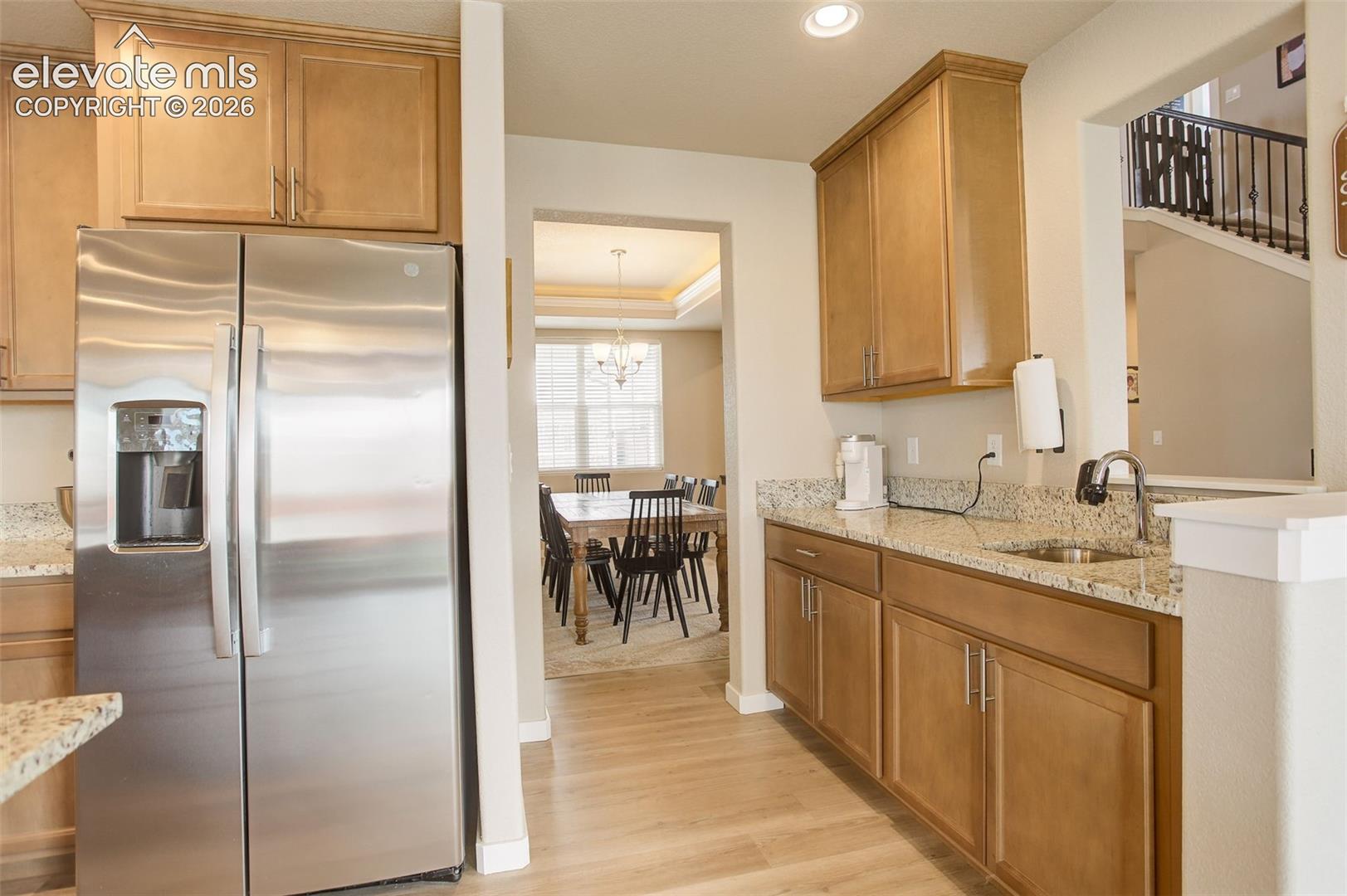 Kitchen featuring stainless steel refrigerator with ice dispenser, light stone counters, wood finish cabinetry, light wood finished floors, and a tray ceiling, coffee bar, or wet bar with sink, prep sink and additional cabinets.