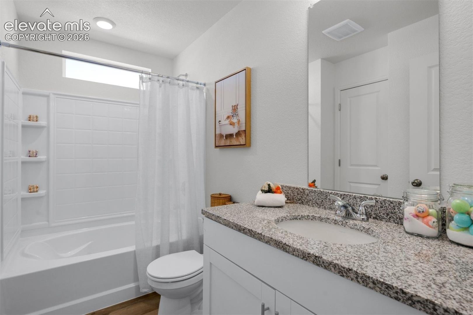White shower/tub combination with integrated shelving, transom window, recessed lighting, wood-finish flooring, and a vanity with a granite countertop
*photos of a model home*