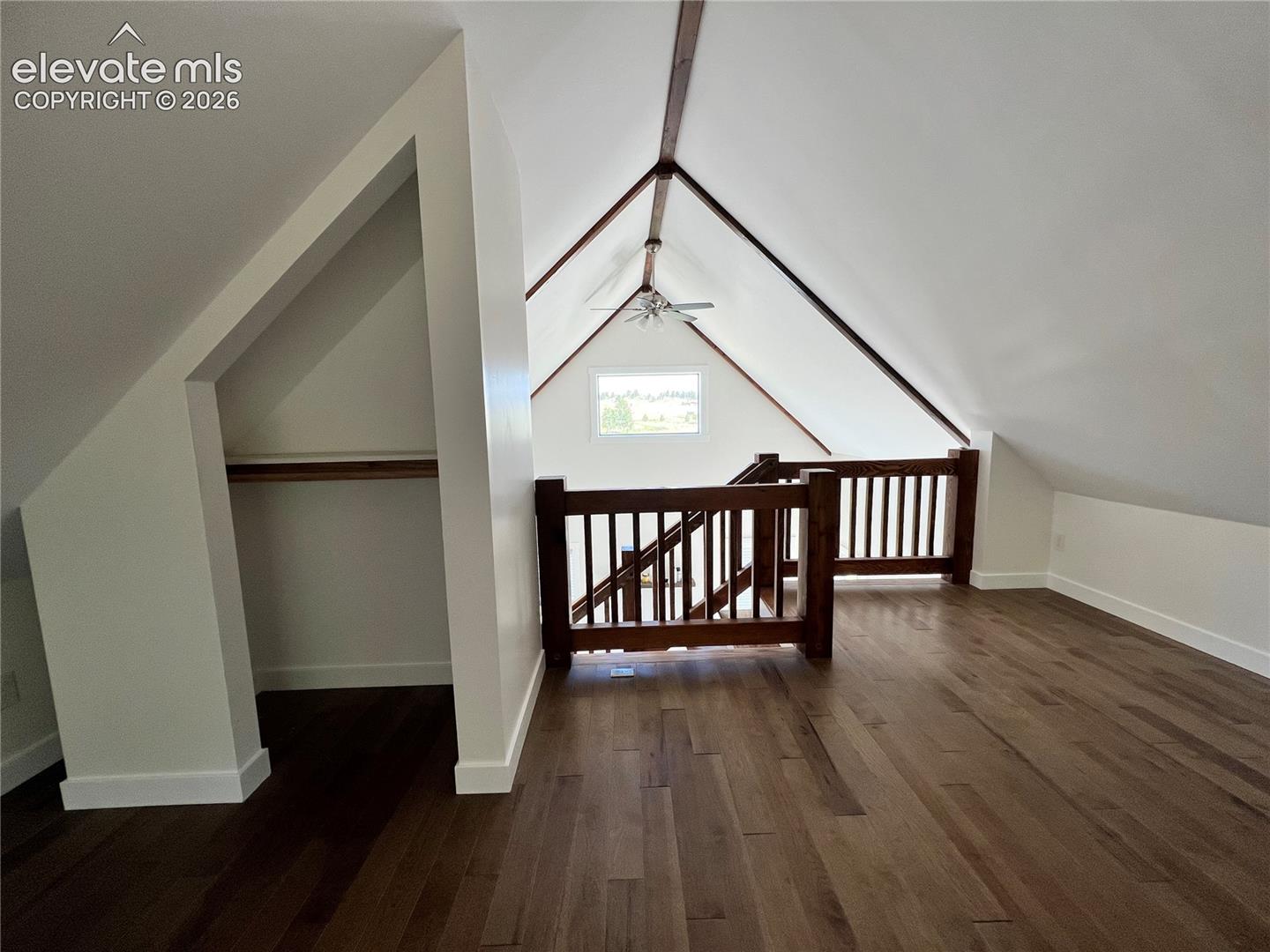 Vaulted ceilings with exposed beams, rich wood-finish flooring, built-in storage alcove, and a window providing natural light
