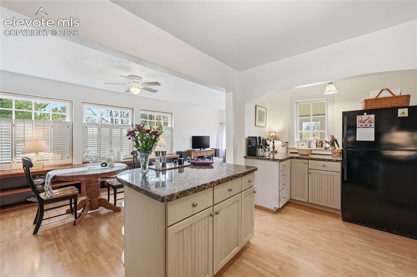 Kitchen featuring stone-surface countertops, beadboard-style cabinetry, an island with built-in storage, wood-finish flooring, and multi-pane windows with integrated shutters