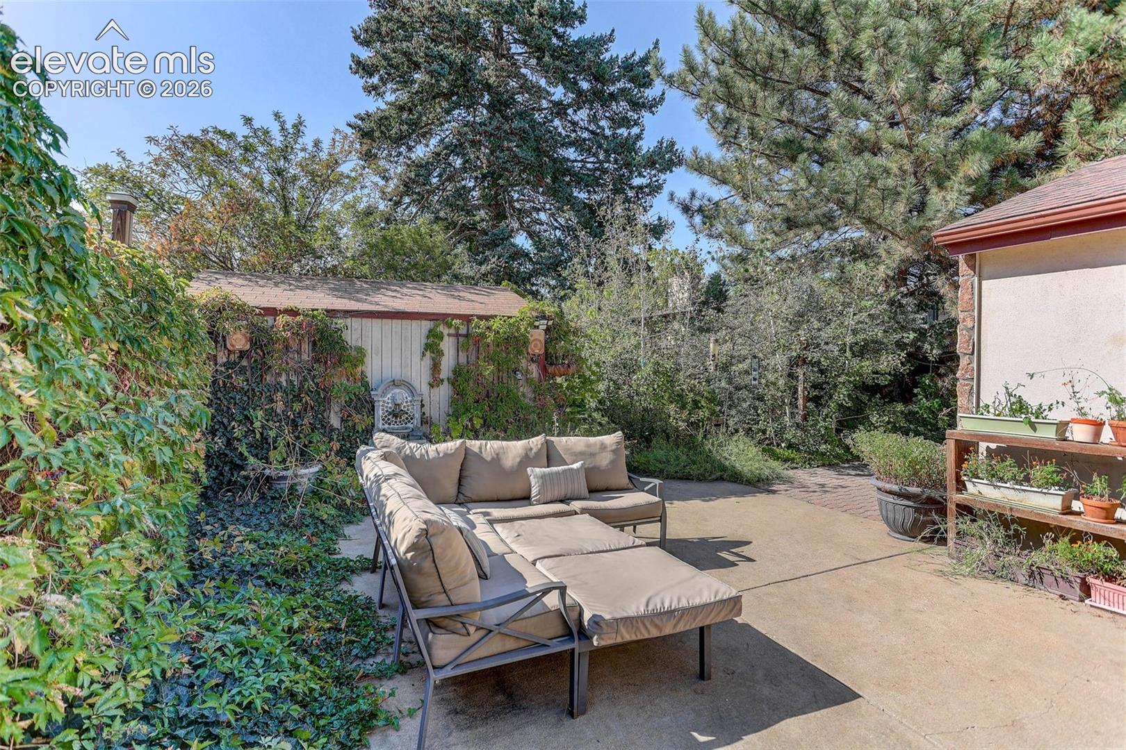 Paved patio area, mature trees, built-in shelving, and a garden shed with a shingle roof