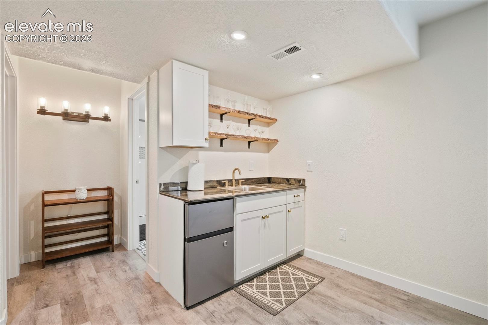 Basement: Wet bar featuring a compact refrigerator, single basin sink with a gold-tone faucet, and white cabinetry