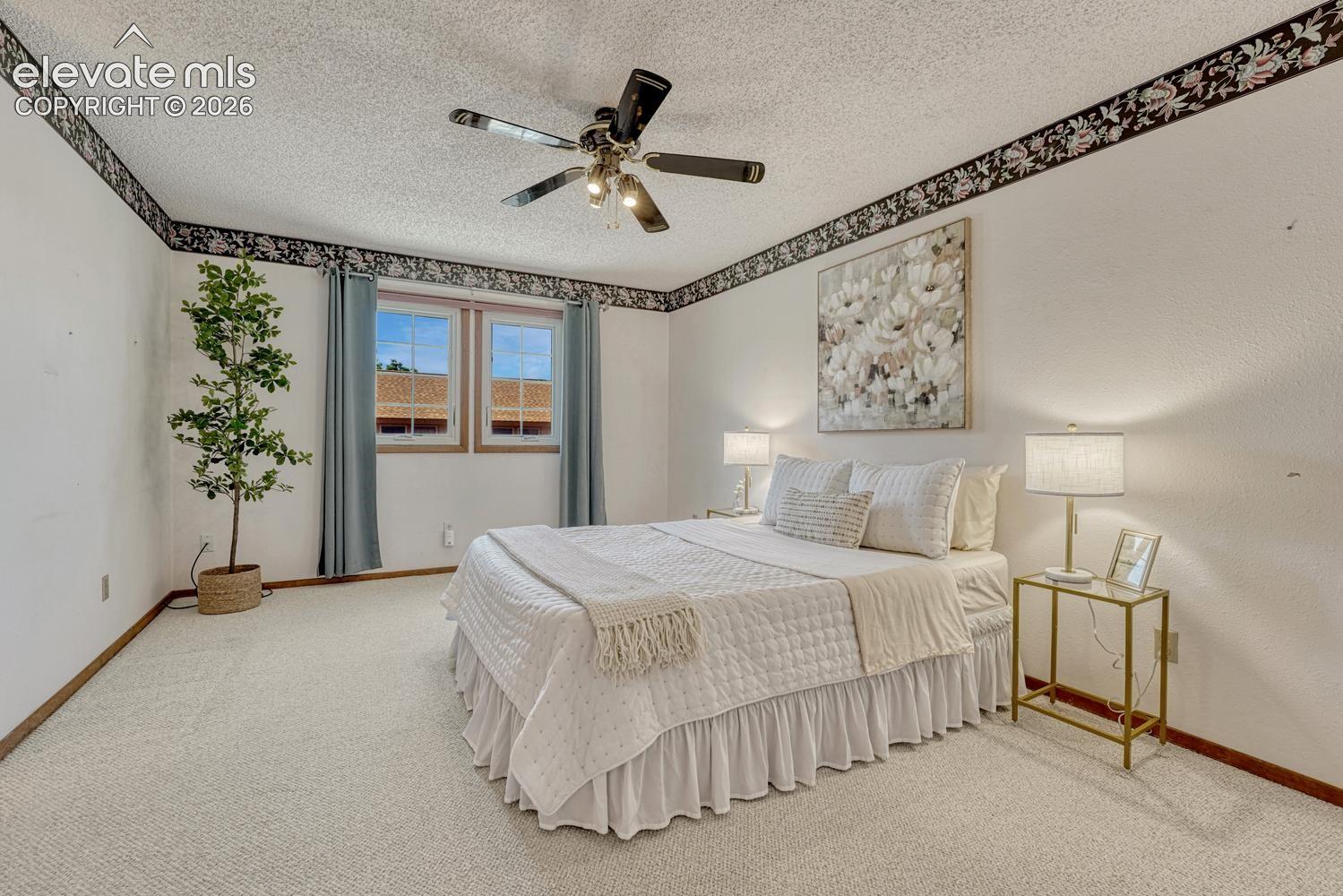 The spacious upper level primary bedroom is a private retreat that features neutral carpet and a lighted ceiling fan.