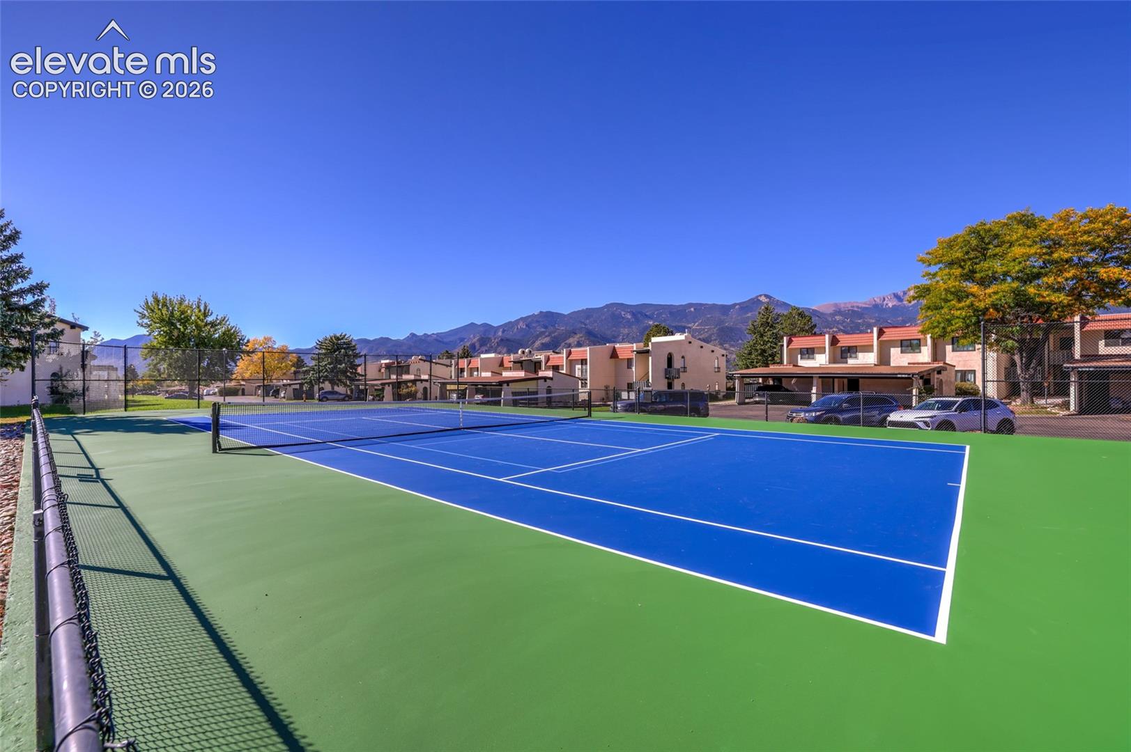 Tennis court with a dual-toned hard surface, perimeter chain-link fencing, and a mountain range backdrop