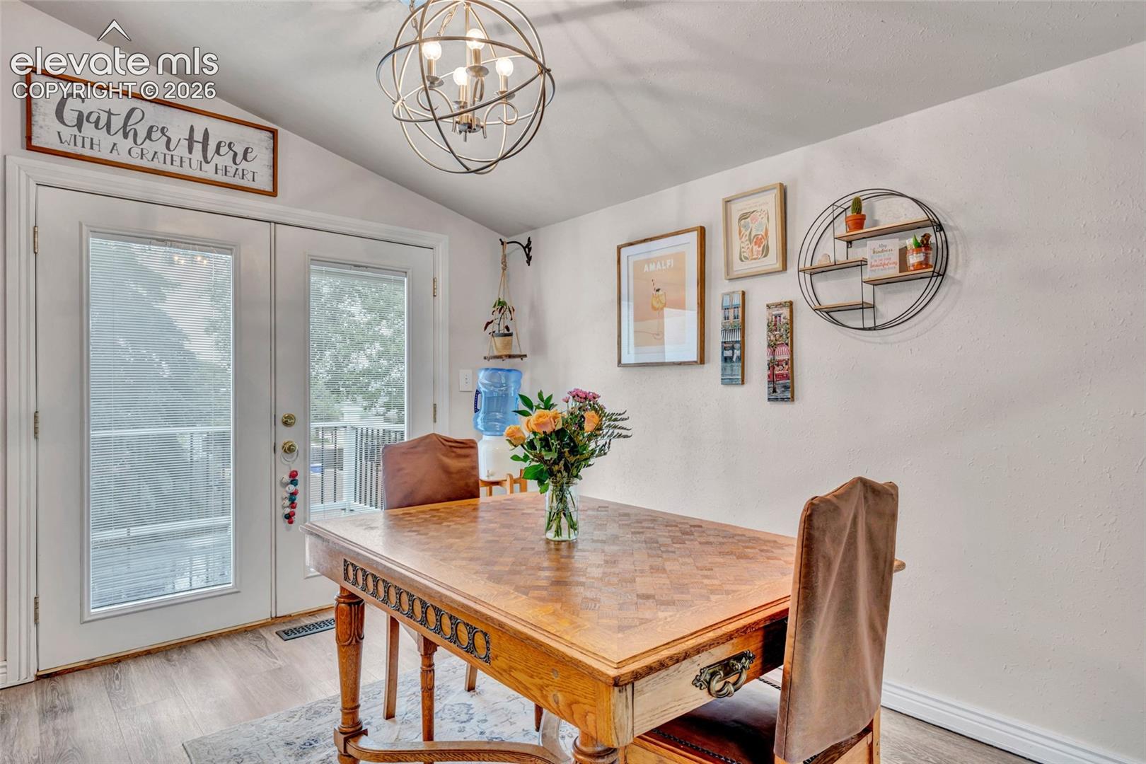 Vaulted ceiling room featuring French doors, wood-finish flooring, and a contemporary orb chandelier