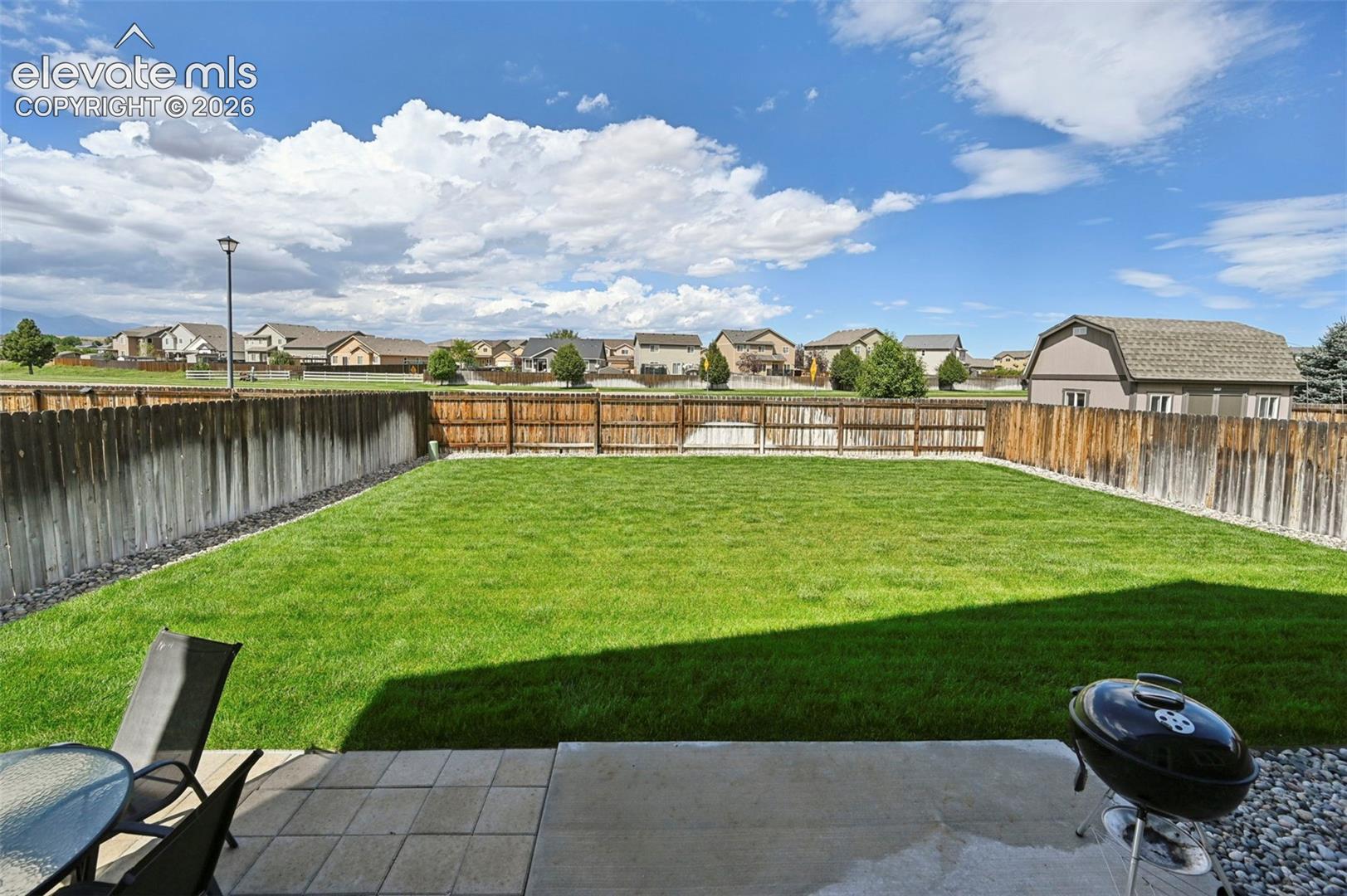 Expansive backyard featuring a manicured lawn, wood fencing, and a concrete patio