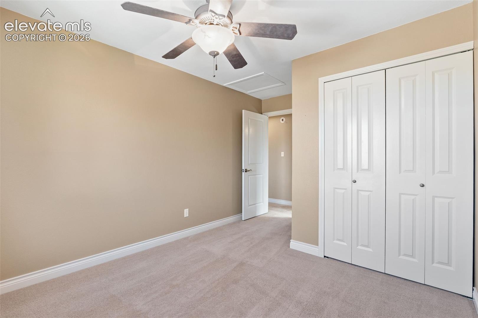 Neutral-toned interior room featuring wall-to-wall carpeting, white dual-panel closet doors, and a ceiling-mounted fan with integrated lighting