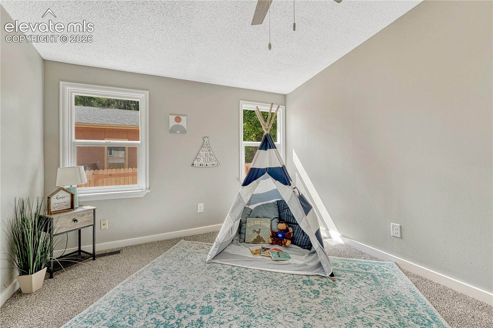 Neutral wall paint, textured ceiling, carpet flooring, two windows, and a ceiling fan