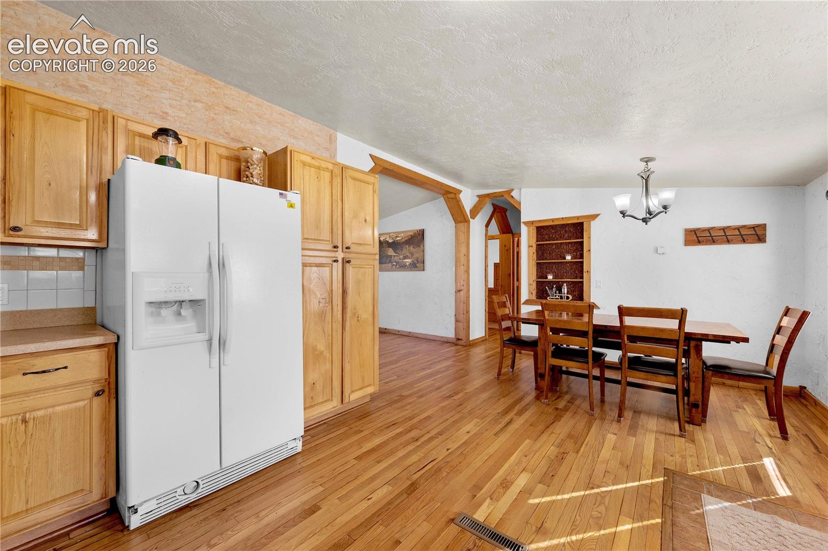 Dining space featuring light hardwood / wood-style flooring, a textured ceiling, vaulted ceiling, and an inviting chandelier