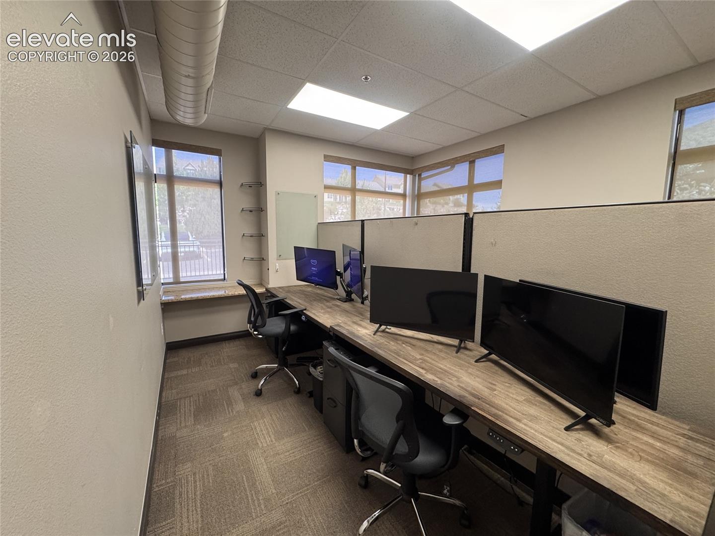 Dedicated office space featuring large windows, wood-finish countertops, modular workstation partitions, recessed lighting, and patterned carpet flooring