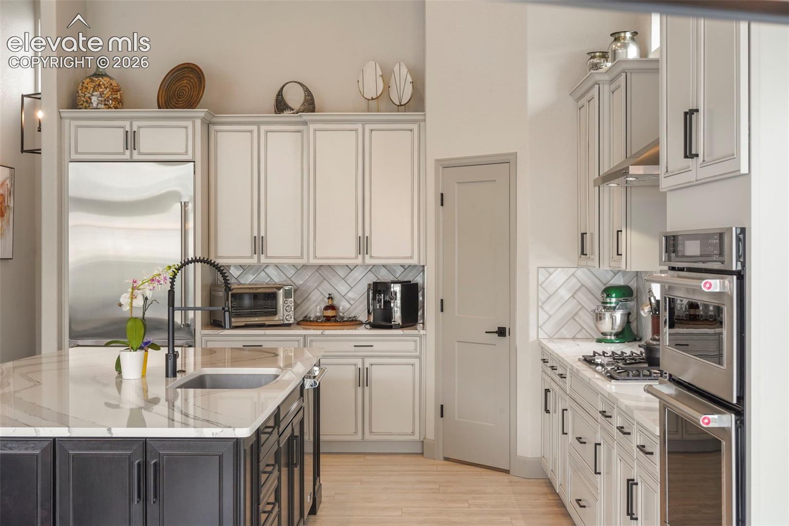 Gourmet kitchen featuring a central island with an undermount sink, marble-finish countertops, stainless steel appliances, herringbone tile backsplash, and light wood-finish flooring
