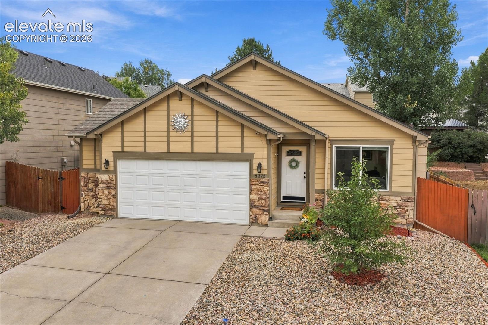 Tan home with stone accents, a white double garage door, and a gravel front yard.