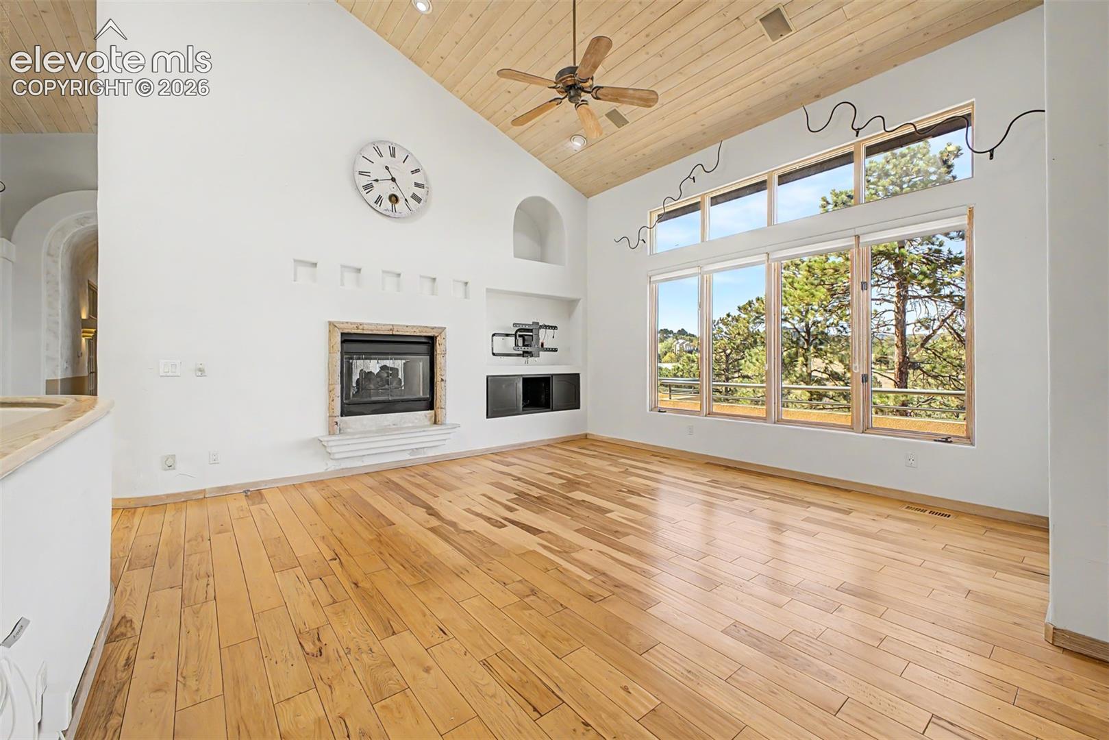 Vaulted wood-paneled ceiling, wood-finish flooring, built-in fireplace, expansive window wall, and ceiling fan