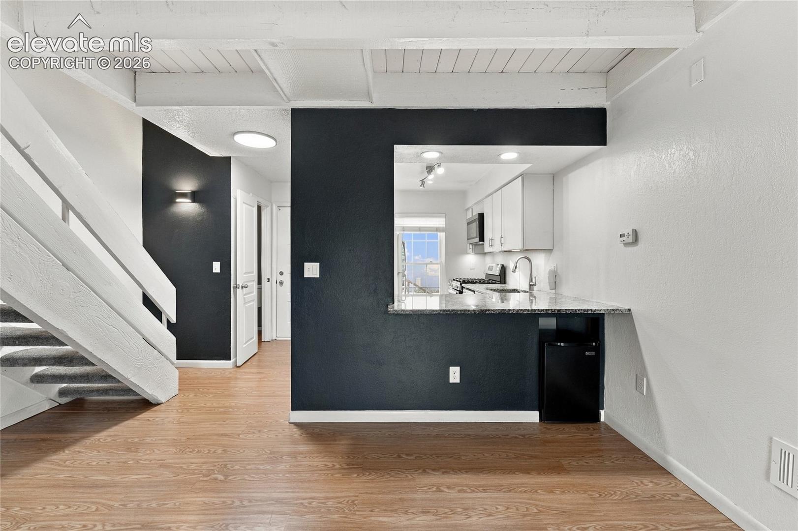 Wood-finish flooring, exposed beam ceiling, breakfast bar with stone-surfaced countertop, and staircase with white railings