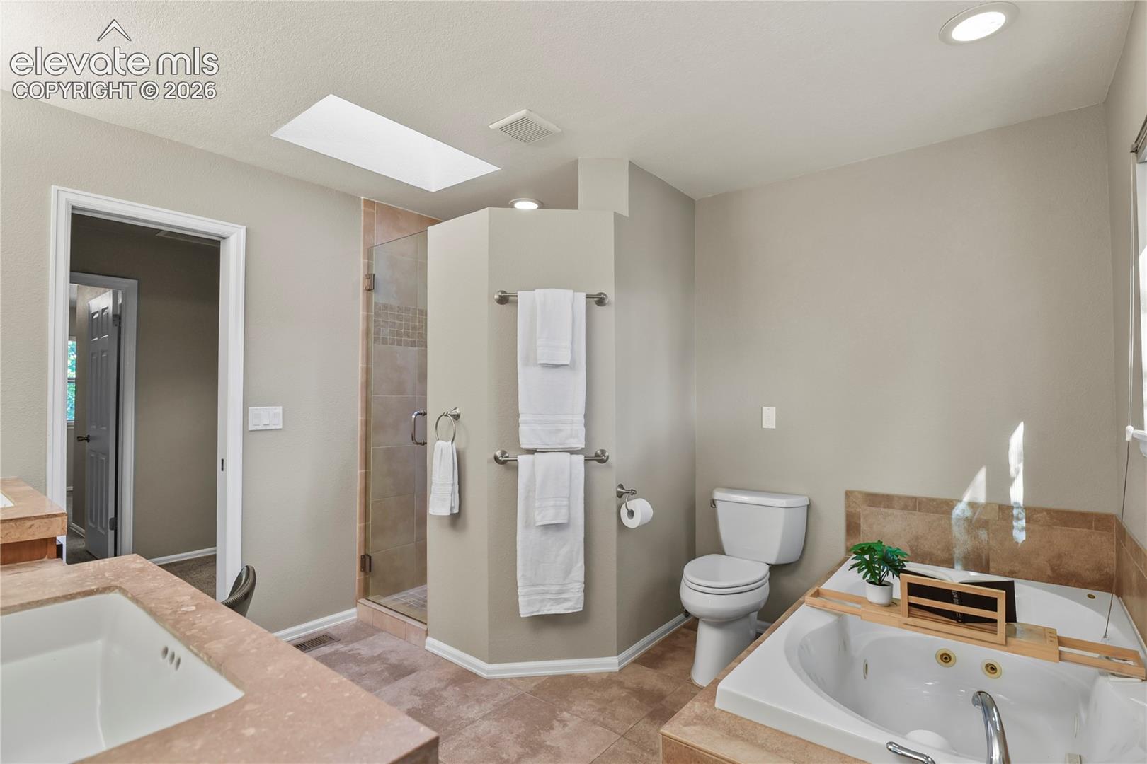 Primary bathroom featuring a built-in jetted tub with tiled surround, enclosed glass shower, recessed lighting, and a skylight