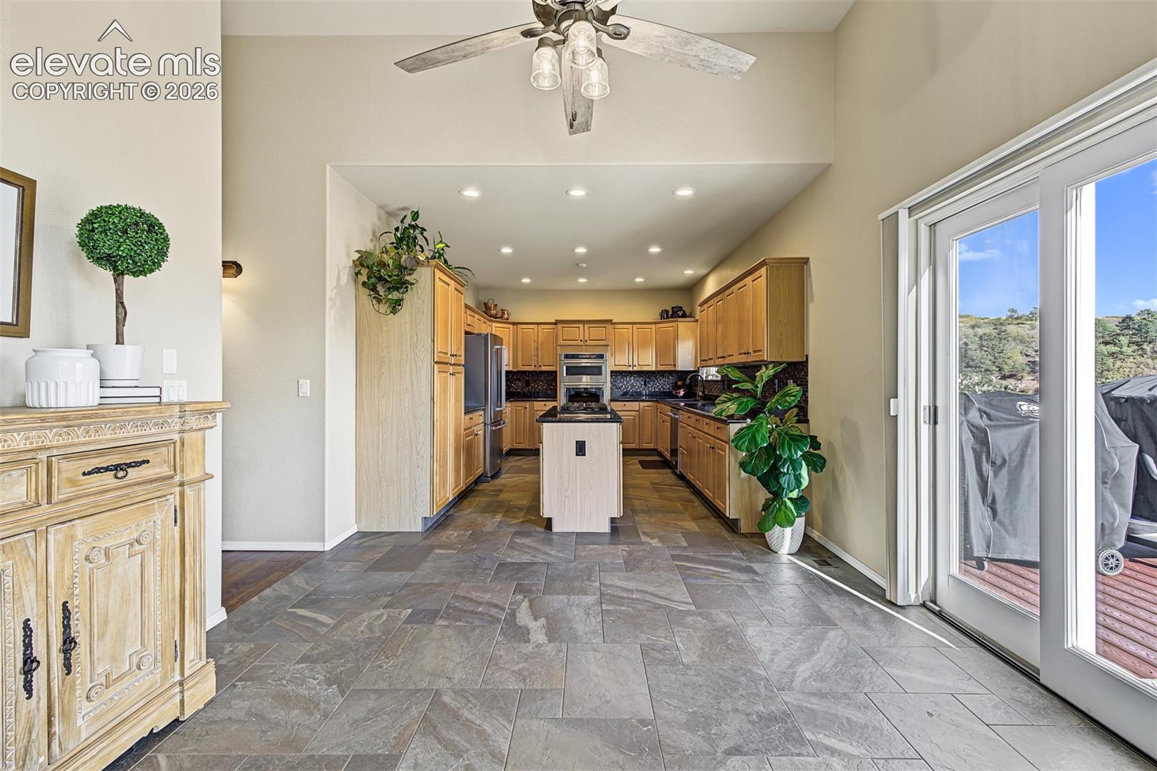 View from the dining area into the kitchen and additional dining space, ideal for a breakfast nook, with tile flooring, a ceiling fan, and sliding glass doors opening to the rear deck.